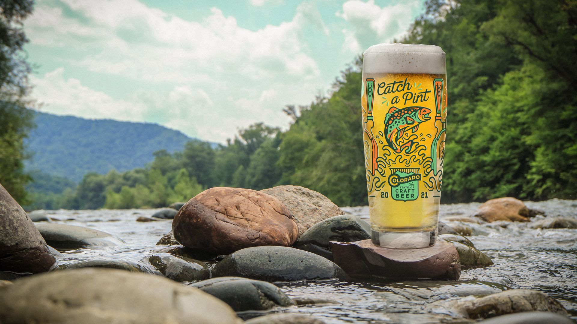 A picture of a colorful pint glass on a rock in the middle of a river.