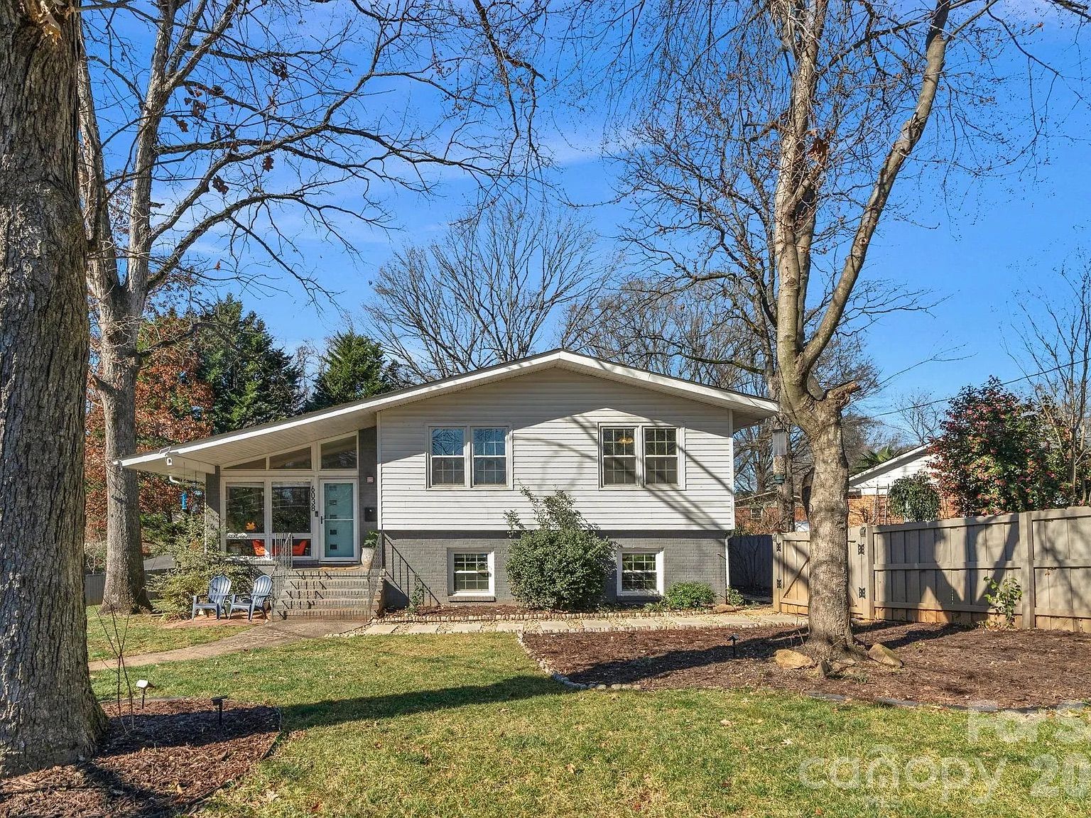 White split-level house with gray foundation, large front windows, and a light blue door, surrounded by bare trees and a green lawn under a clear blue sky.