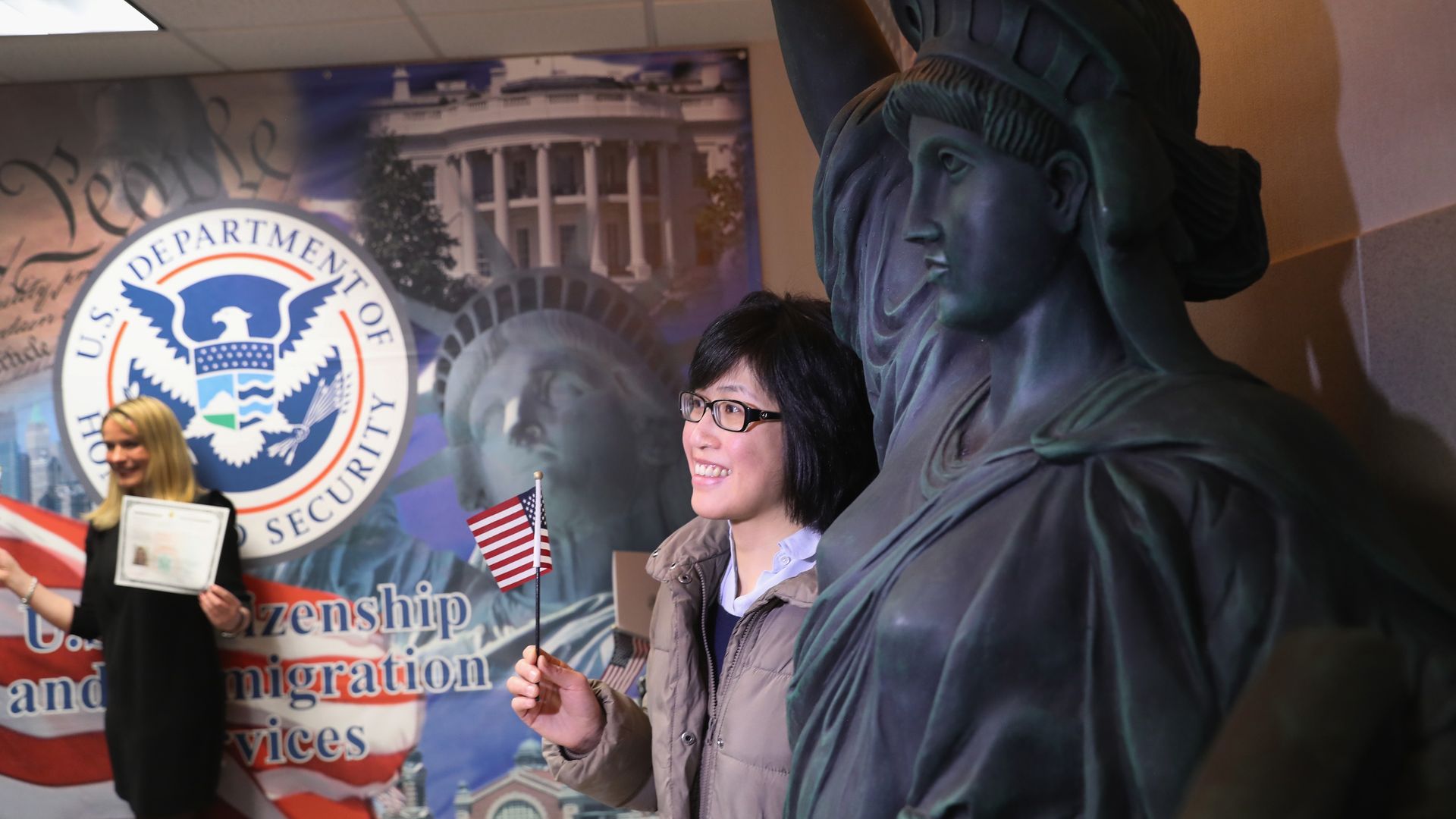New citizens pose for photos at USCIS with a statue of liberty statue