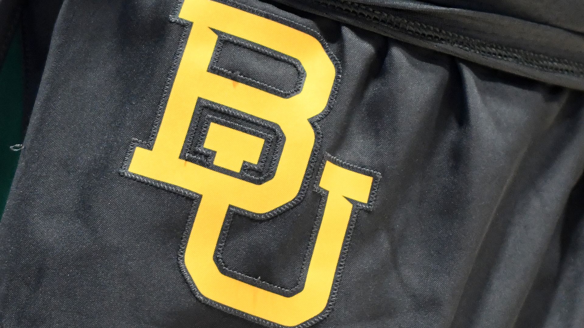 Close-up of black fabric with large yellow embroidered letters "BU" stitched on it, possibly part of a sports or university garment.