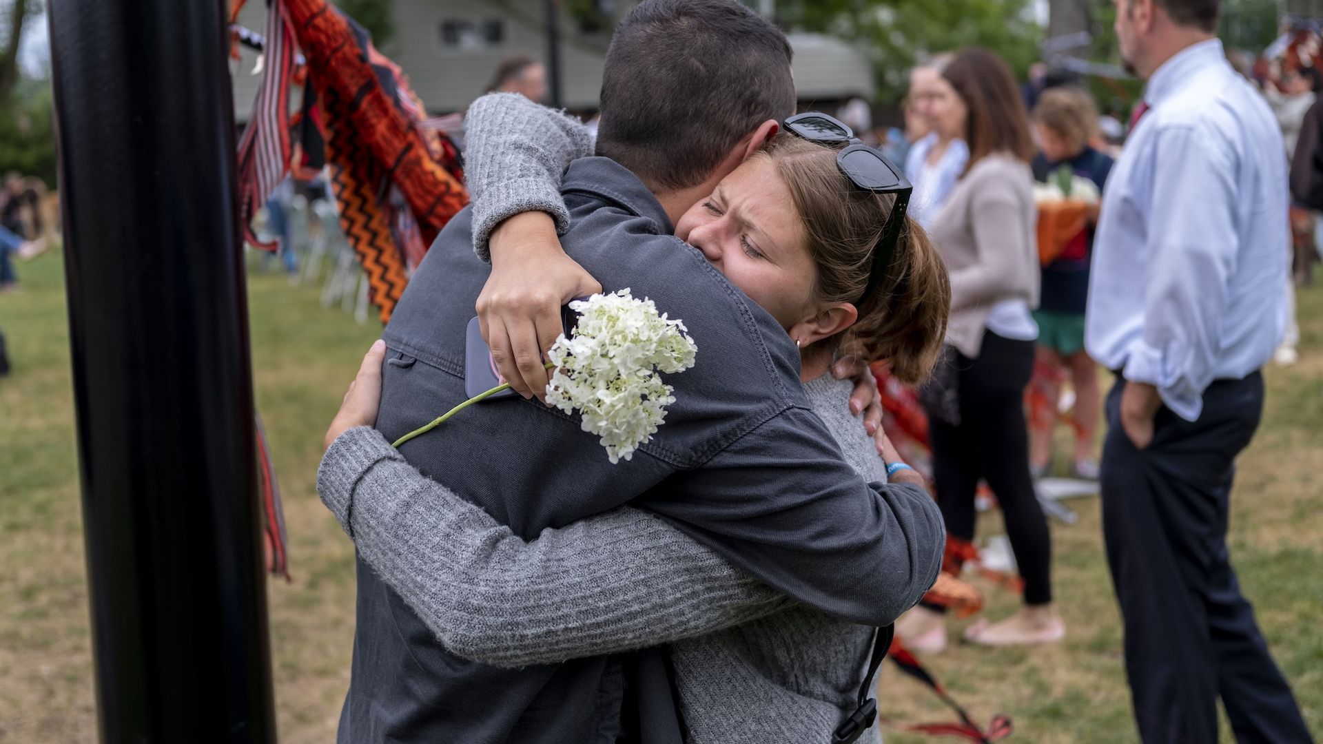 Two people hugging with a woman holding a white flower.