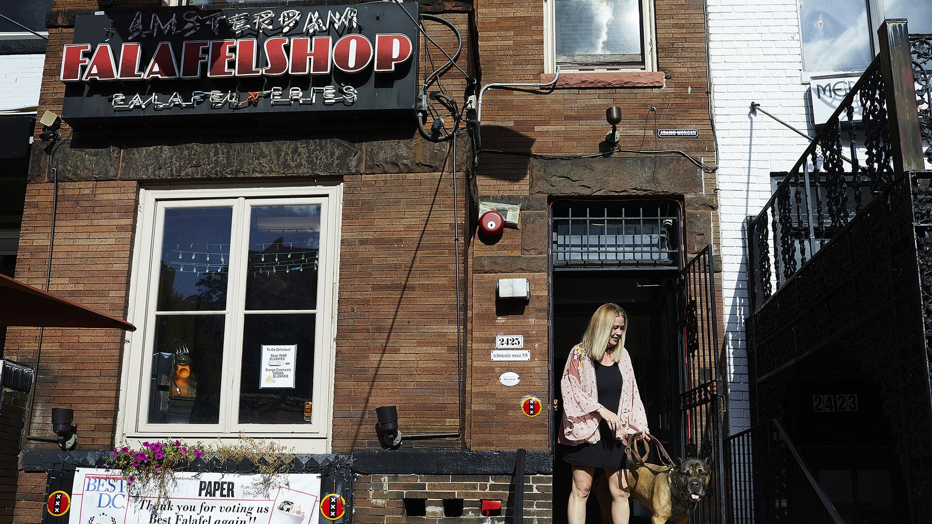 Amsterdam Falafelshop's owner Arianne Bennett stands at the storefront door step with her pet dog.