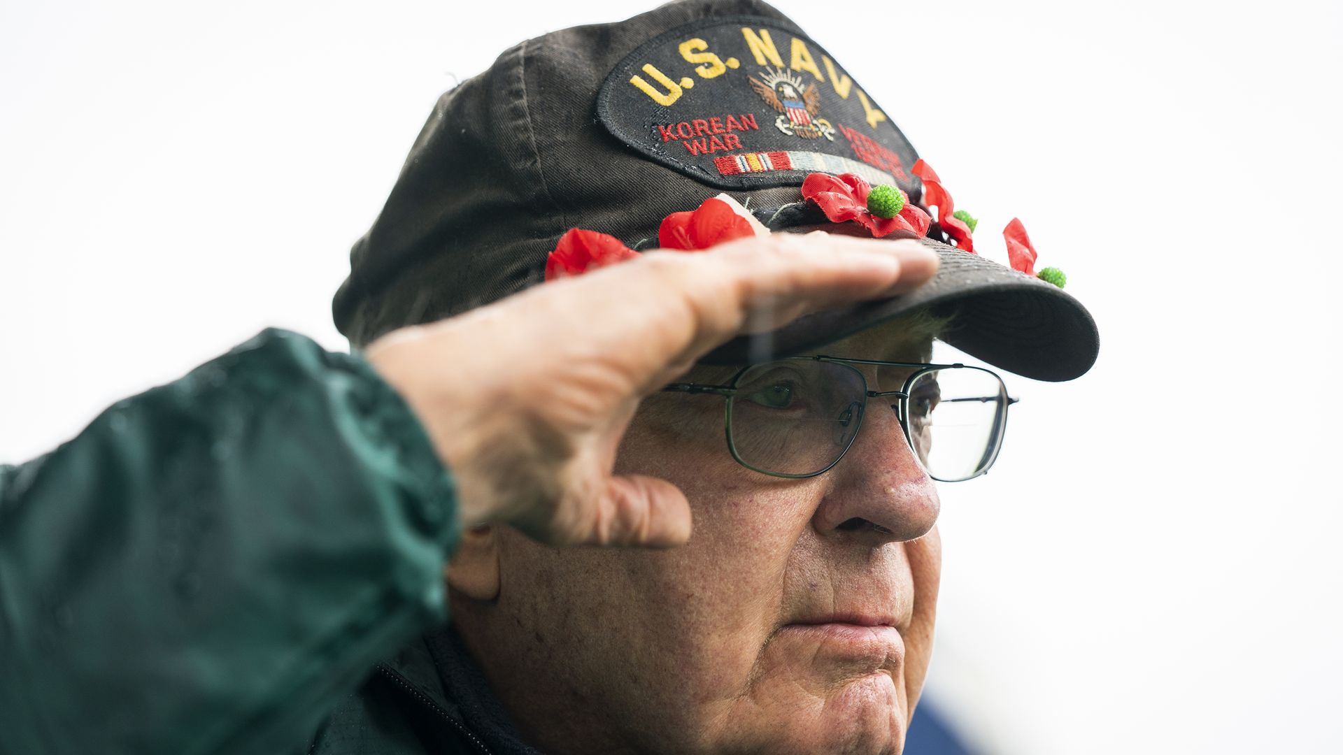 A man wearing a U.S. Navy hat salutes during a ceremony 