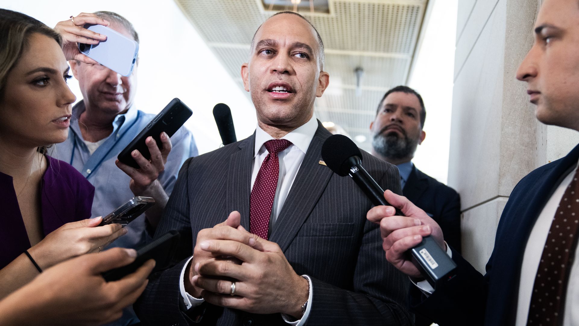 Hakeem Jeffries, wearing a gray pinstripe suit, white shirt and maroon tie, speaks to reporters.