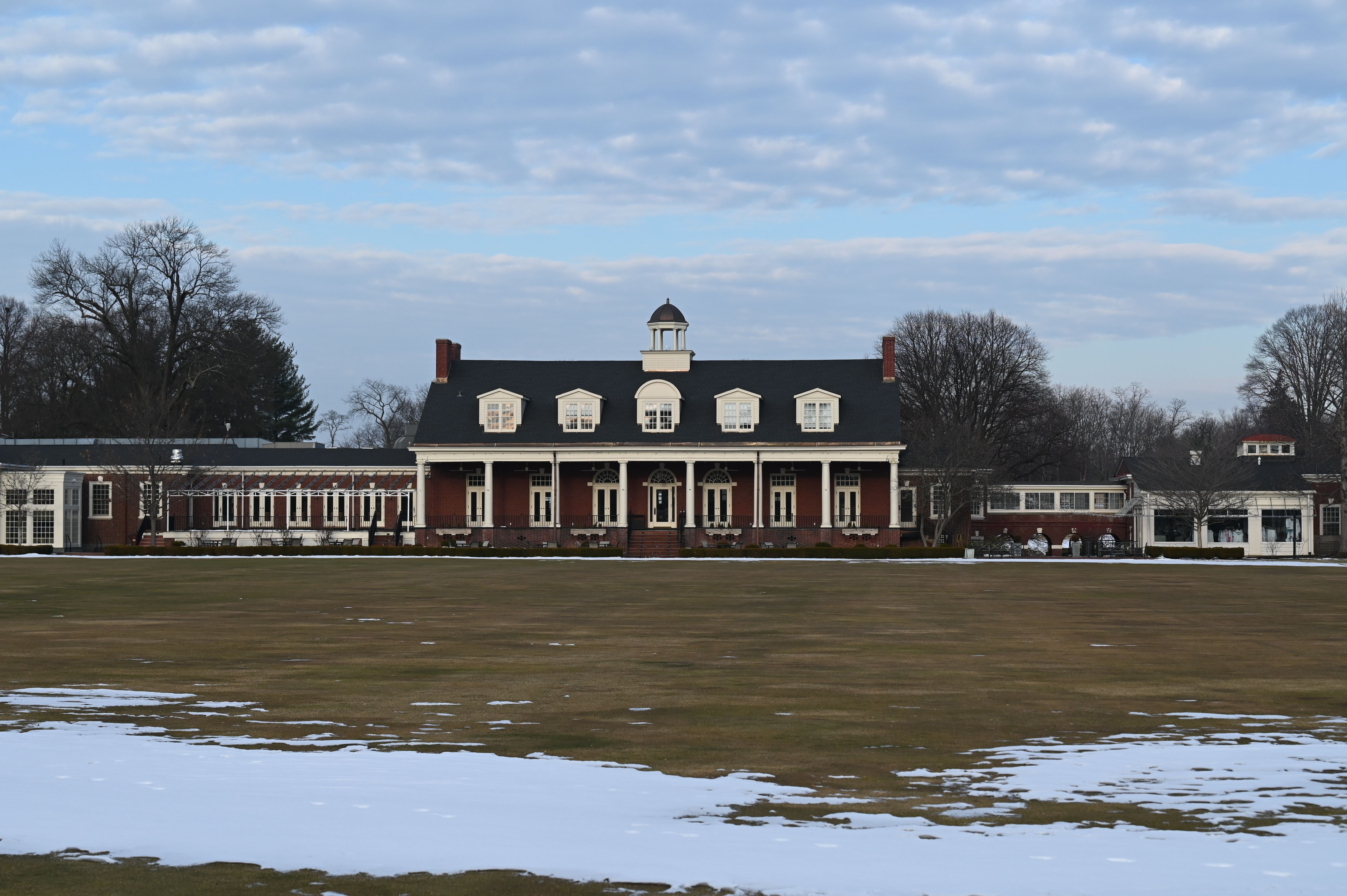 Exterior of the Philadelphia Cricket Club, set behind expansive lawn with patches of snow under a cloudy sky in late winter.