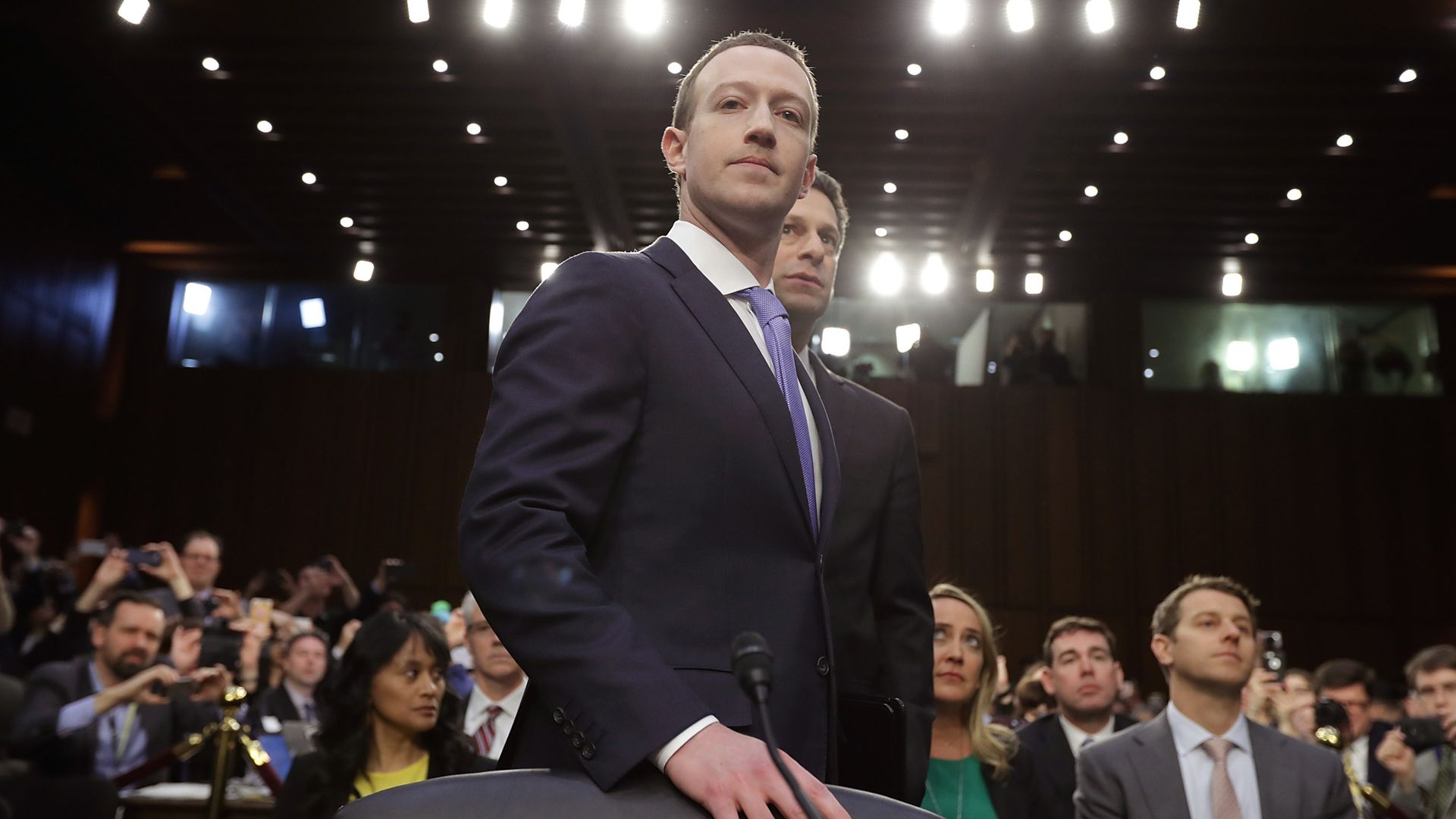 Mark Zuckerberg stands with his hand on a chair