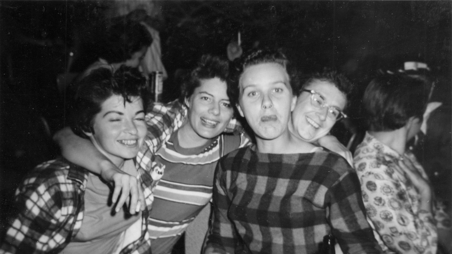 A black and white photograph of three people seated at a table at Jimmie White's Tavern; they're all smiling at the camera and have their arms around each other.