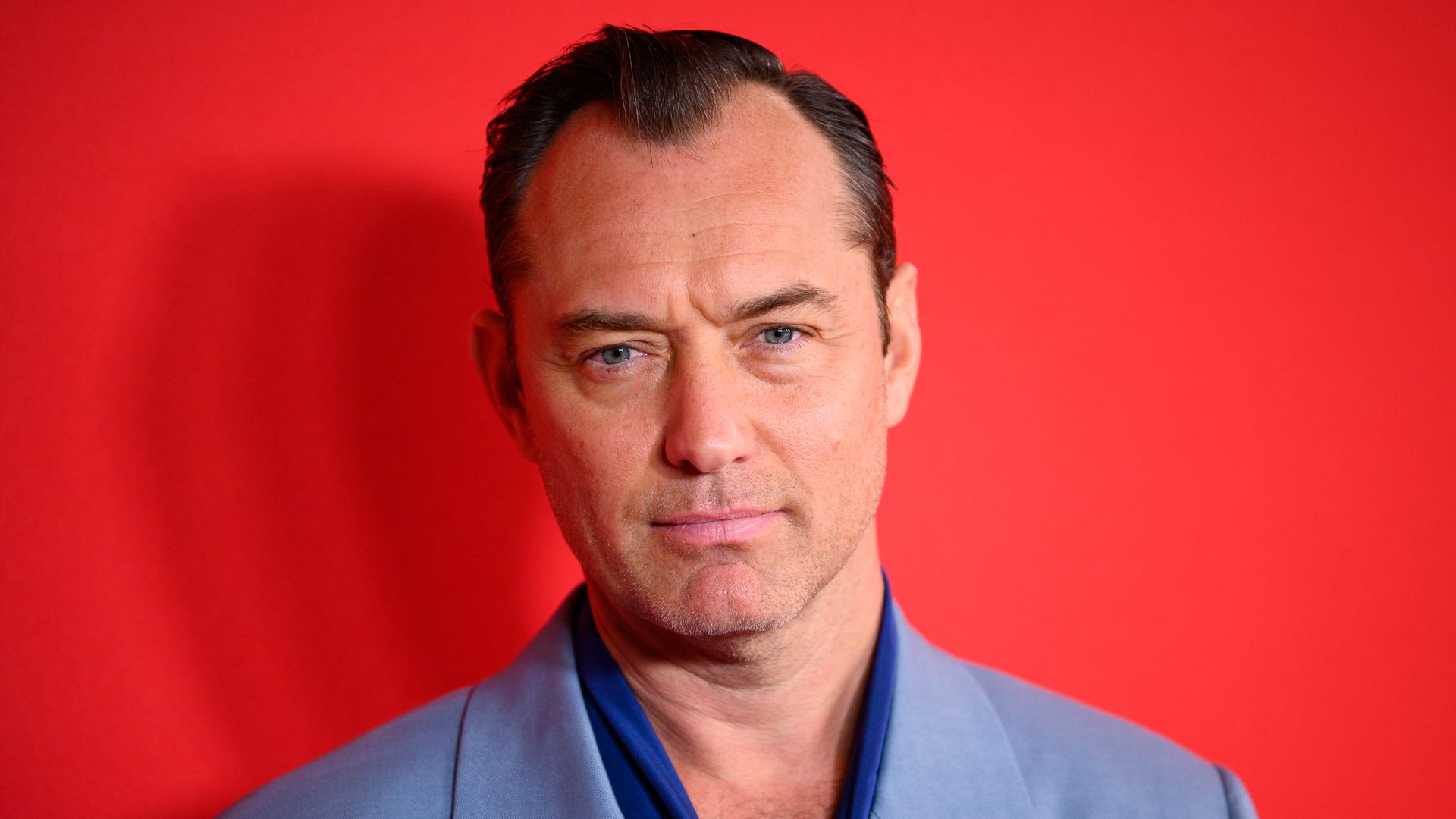 Photo shows a headshot of Jude Law on a red background.