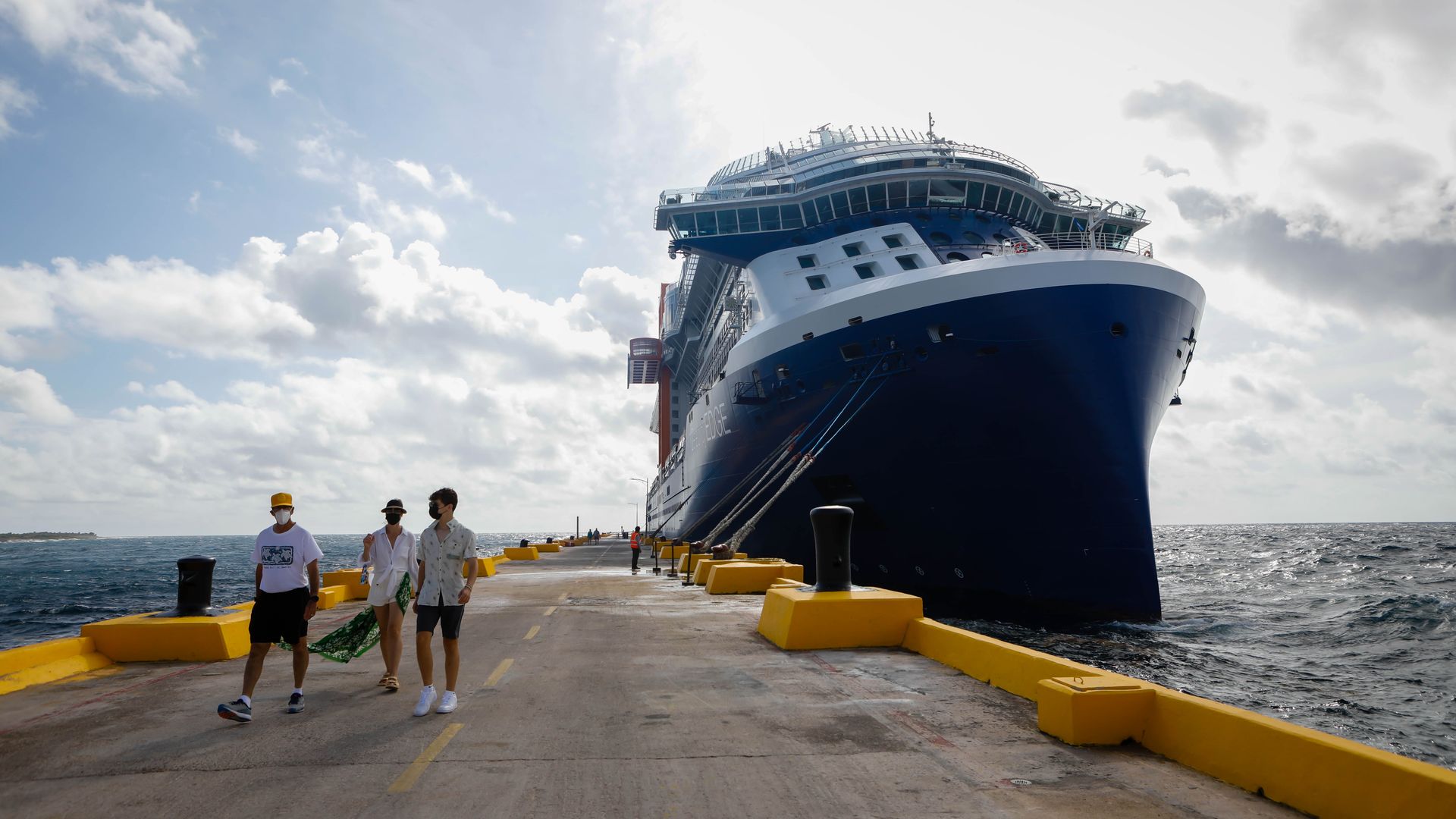 Photo of a blue and white cruise docked at a harbor and three people walking on the deck