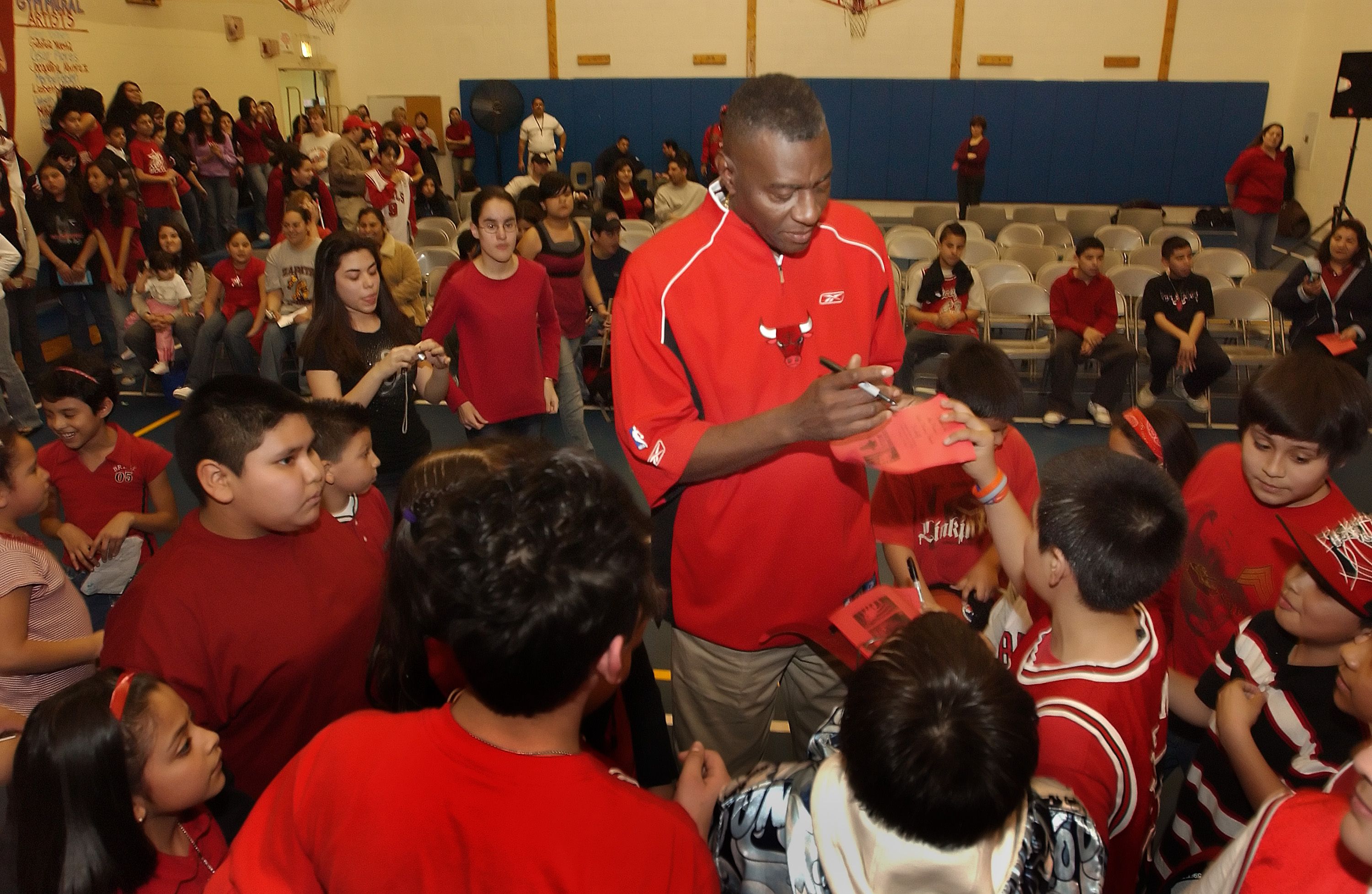 Photo of a man signing autographs for kids in a gym. 