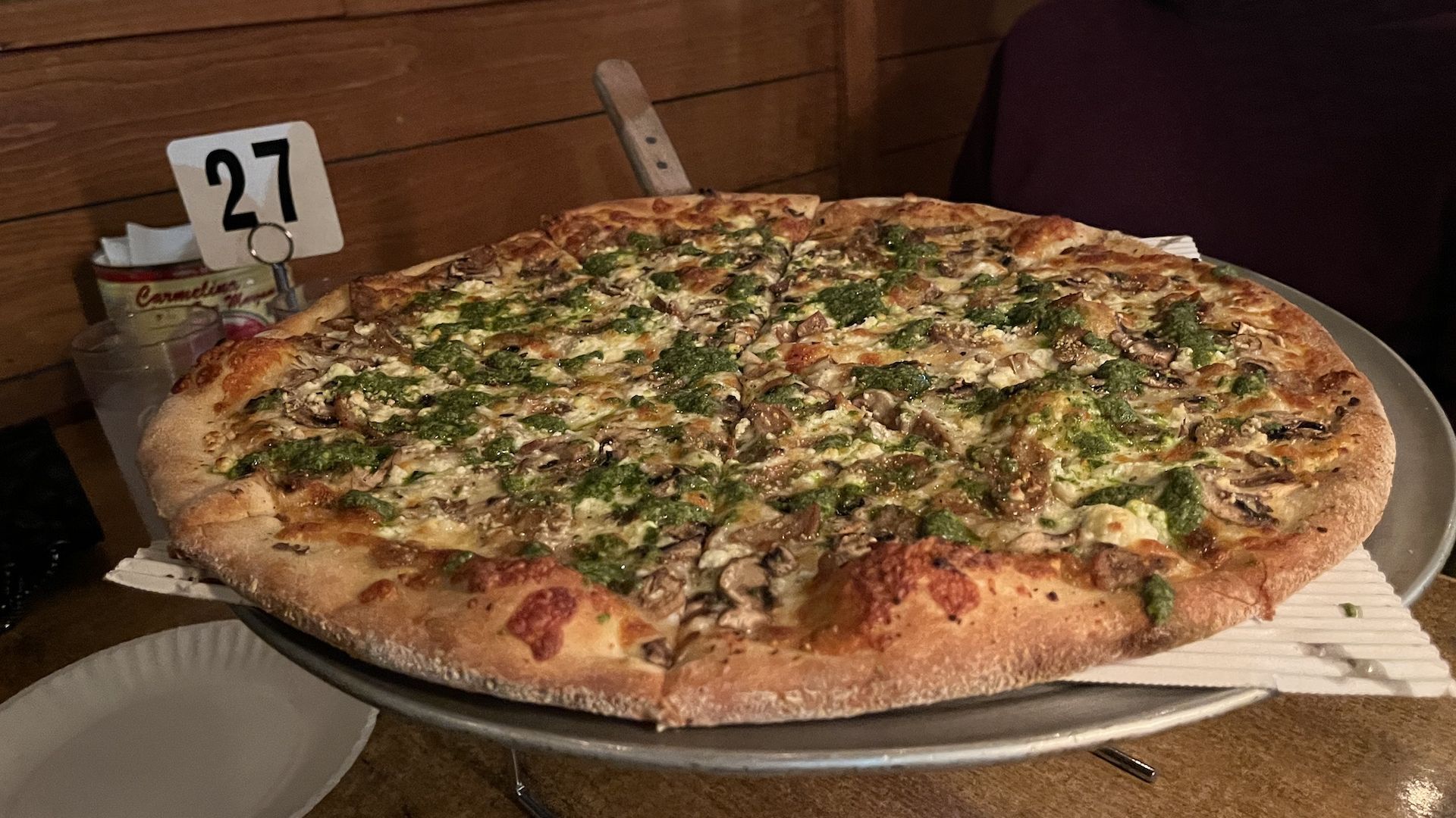 A pizza topped with mushrooms, sausage and pesto on a tray.