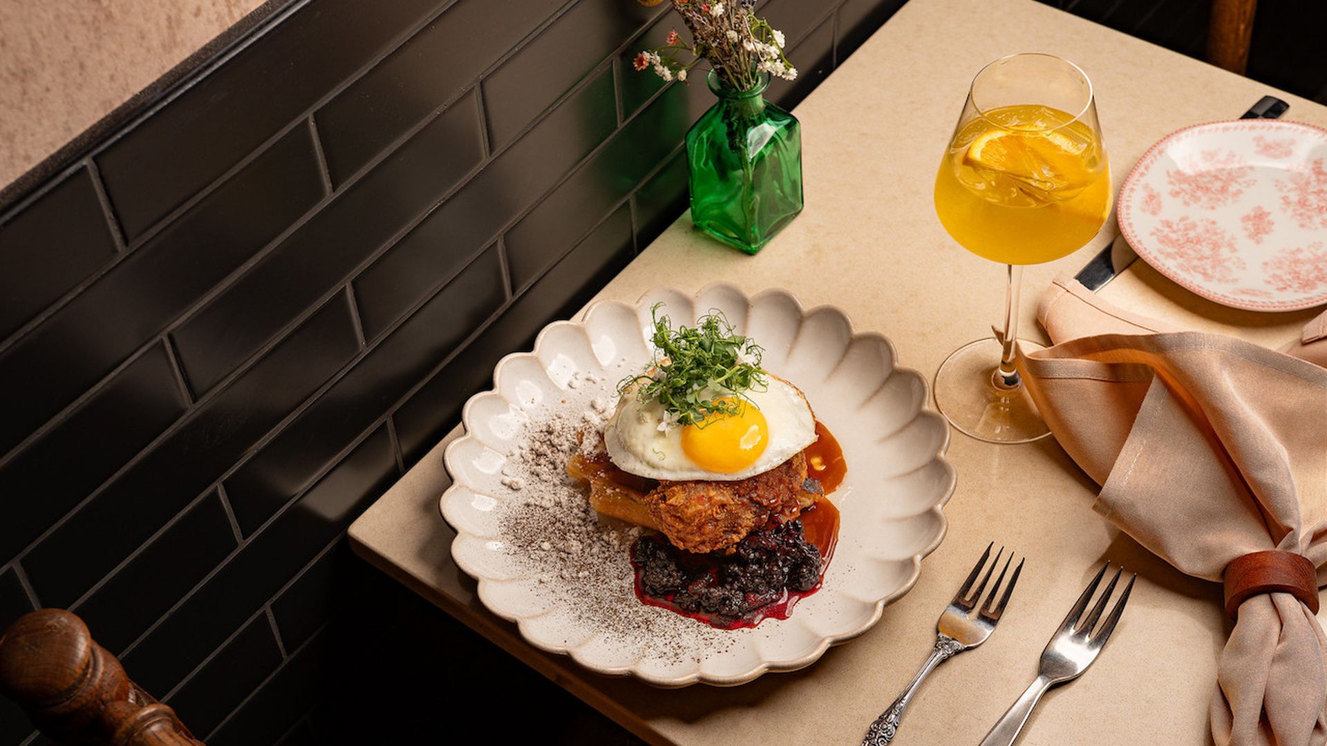 Fried chicken topped with an egg on a table with flowers and a yellow cocktail