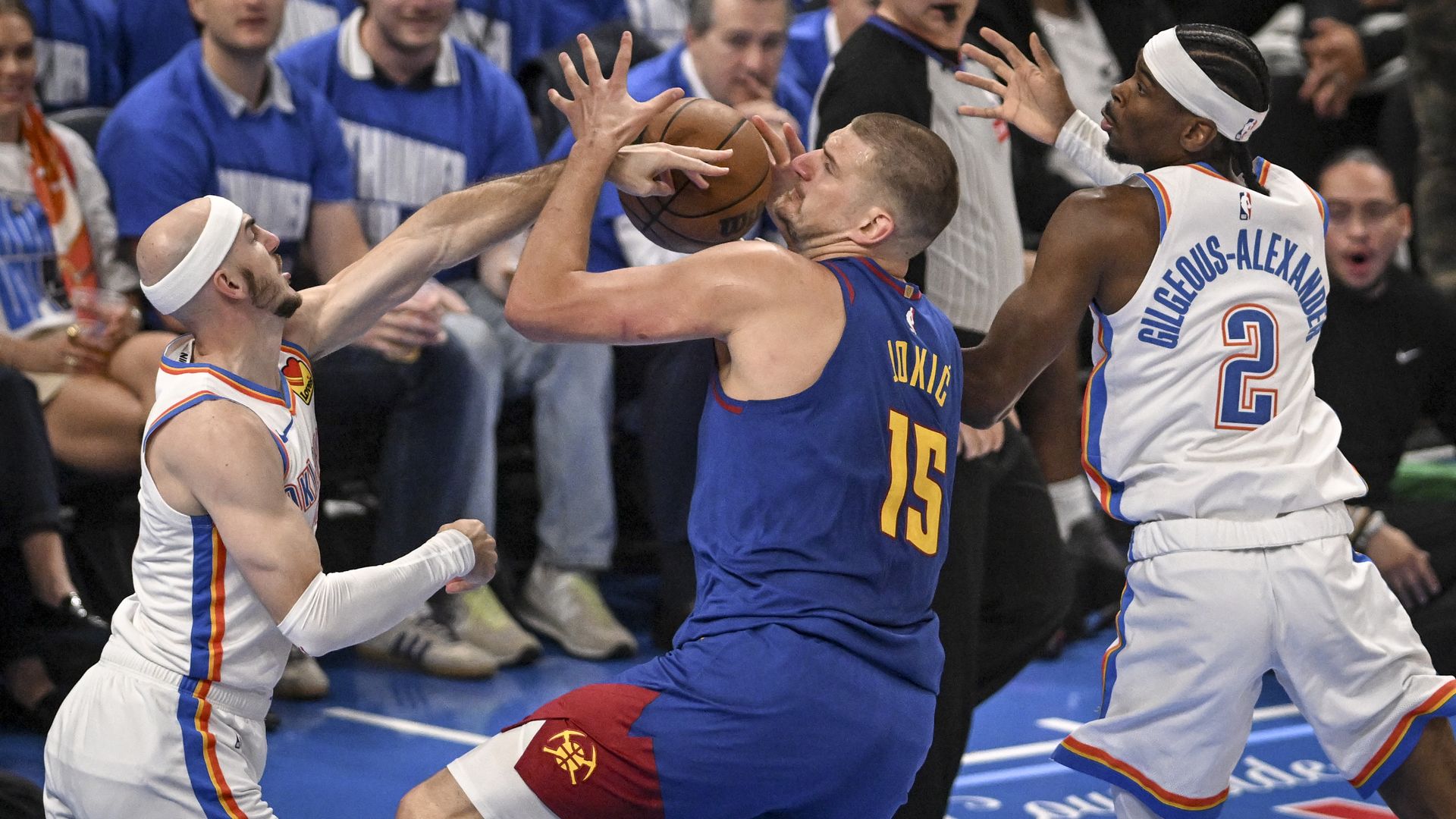 Three basketball players battle for control of the ball. 