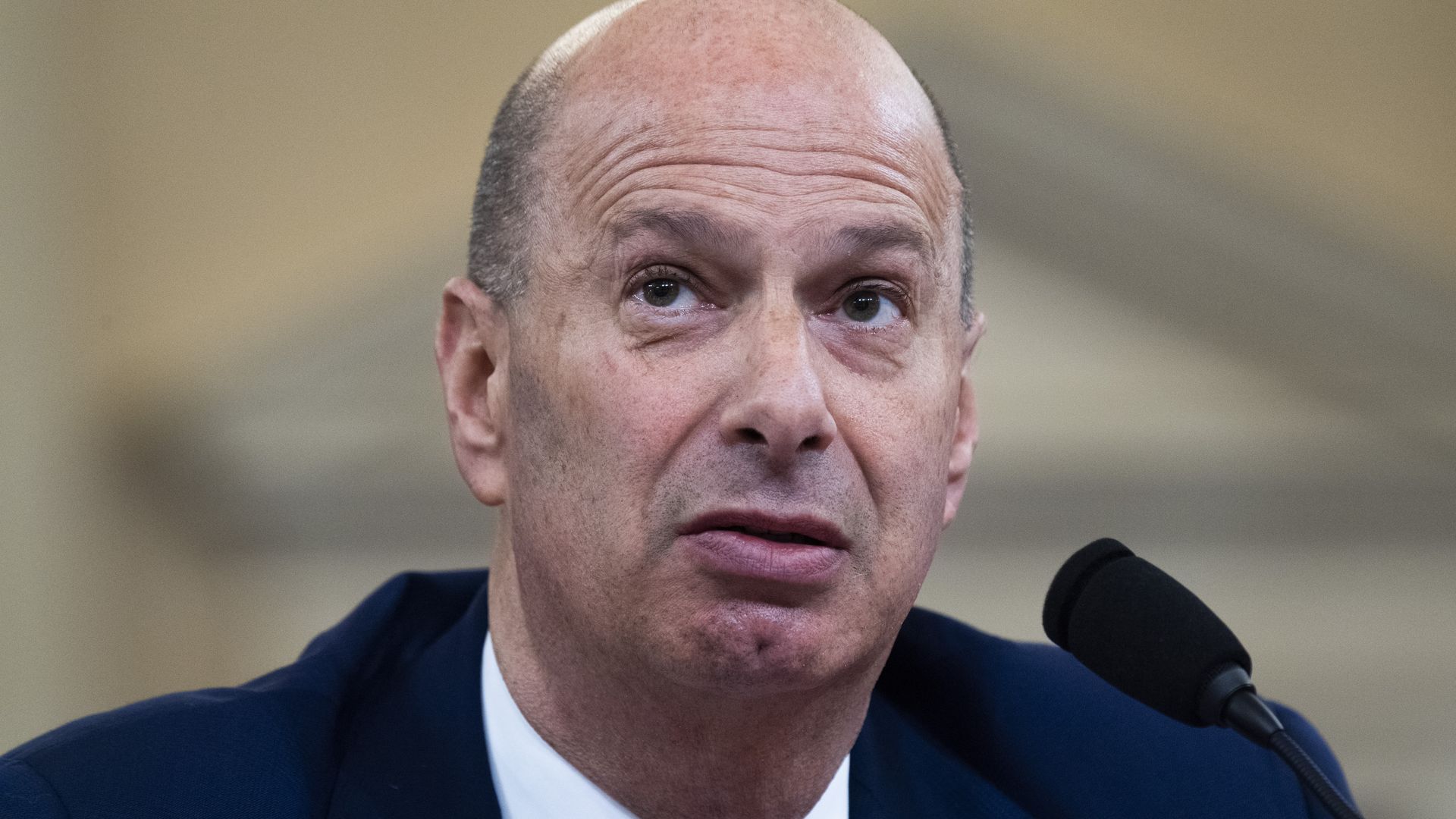 In this image, Gordon Sondland sits in a suit and tie in front of a microphone