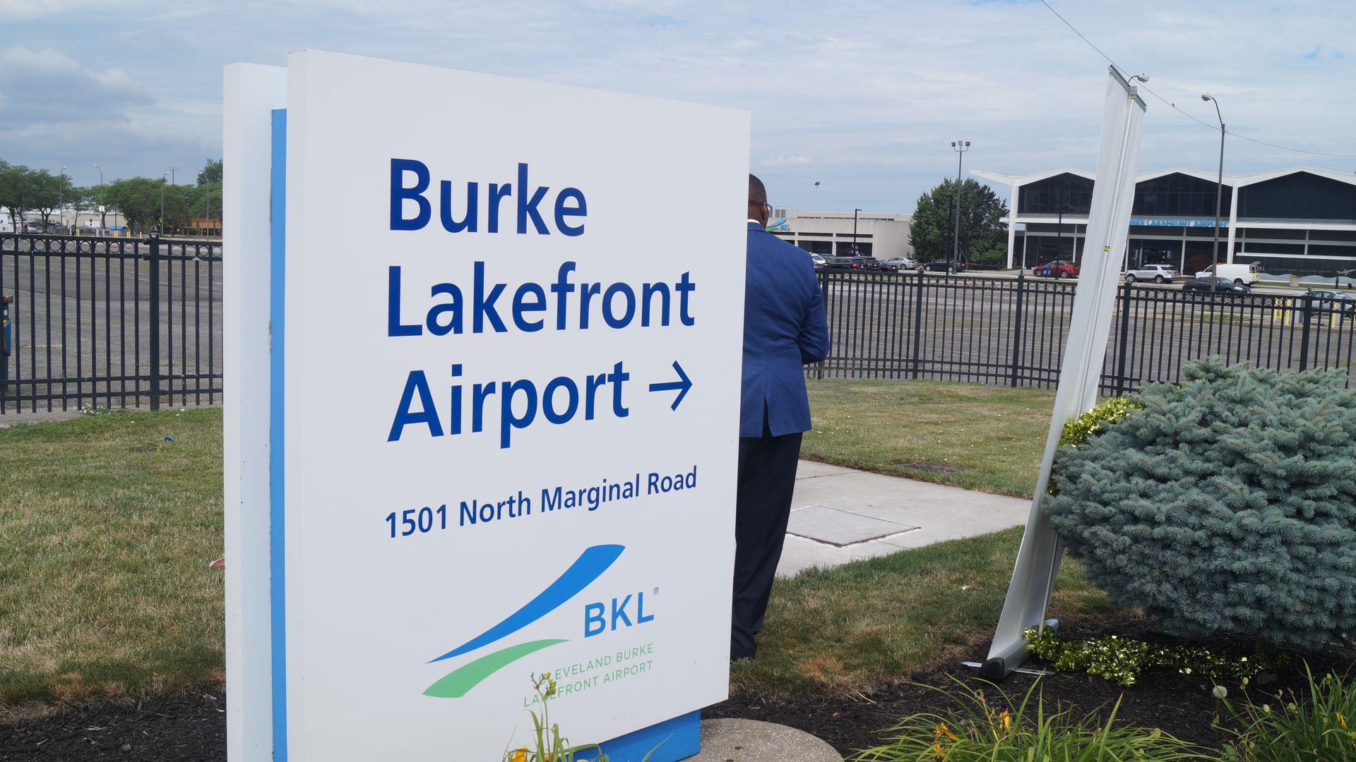 A white sign for Burke Lakefront Airport with blue text in front of the Burke parking lot.