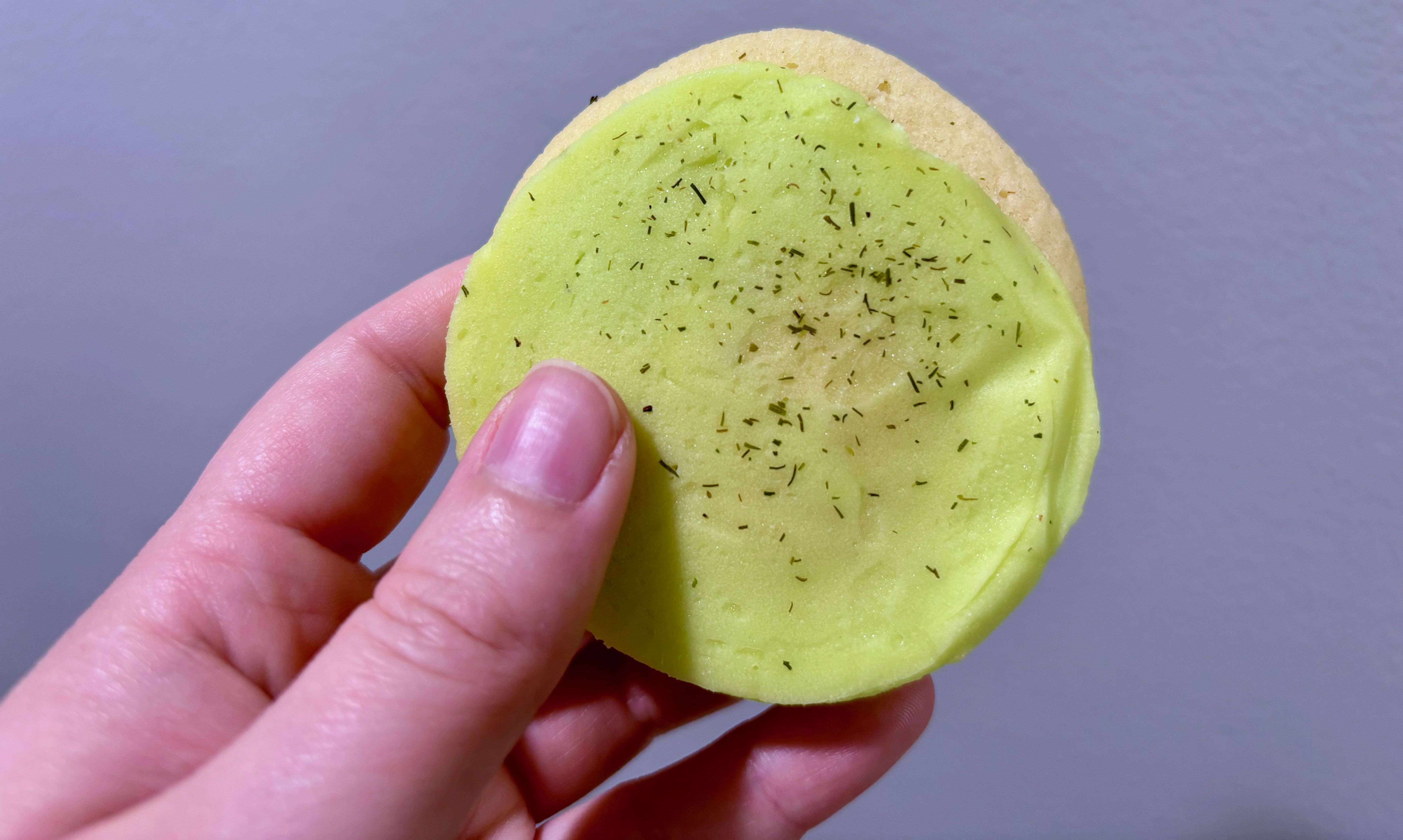 A close-up of a green pickle cookie brushed with dill