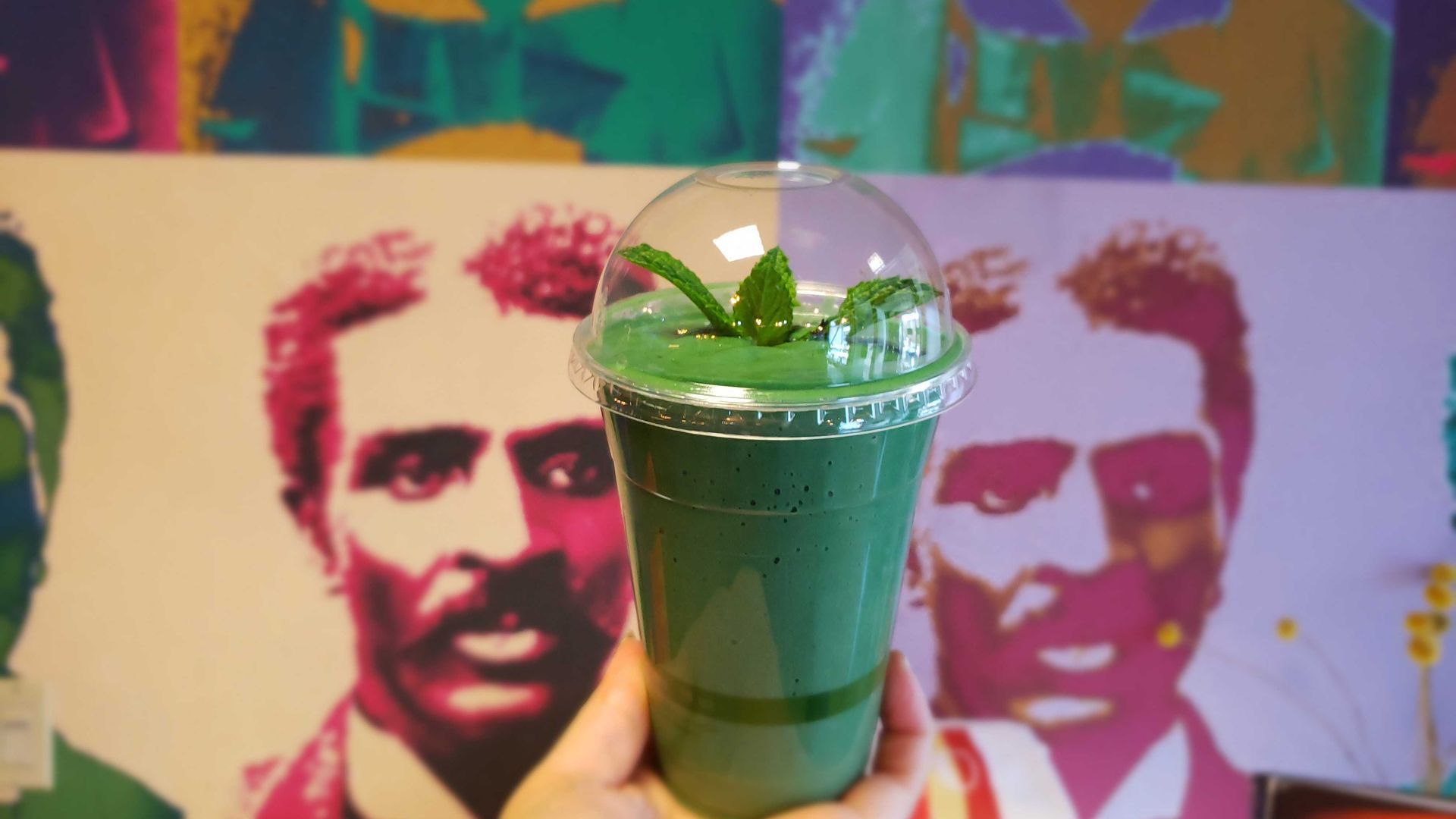 Photo of a smoothie held up against a wall of art.