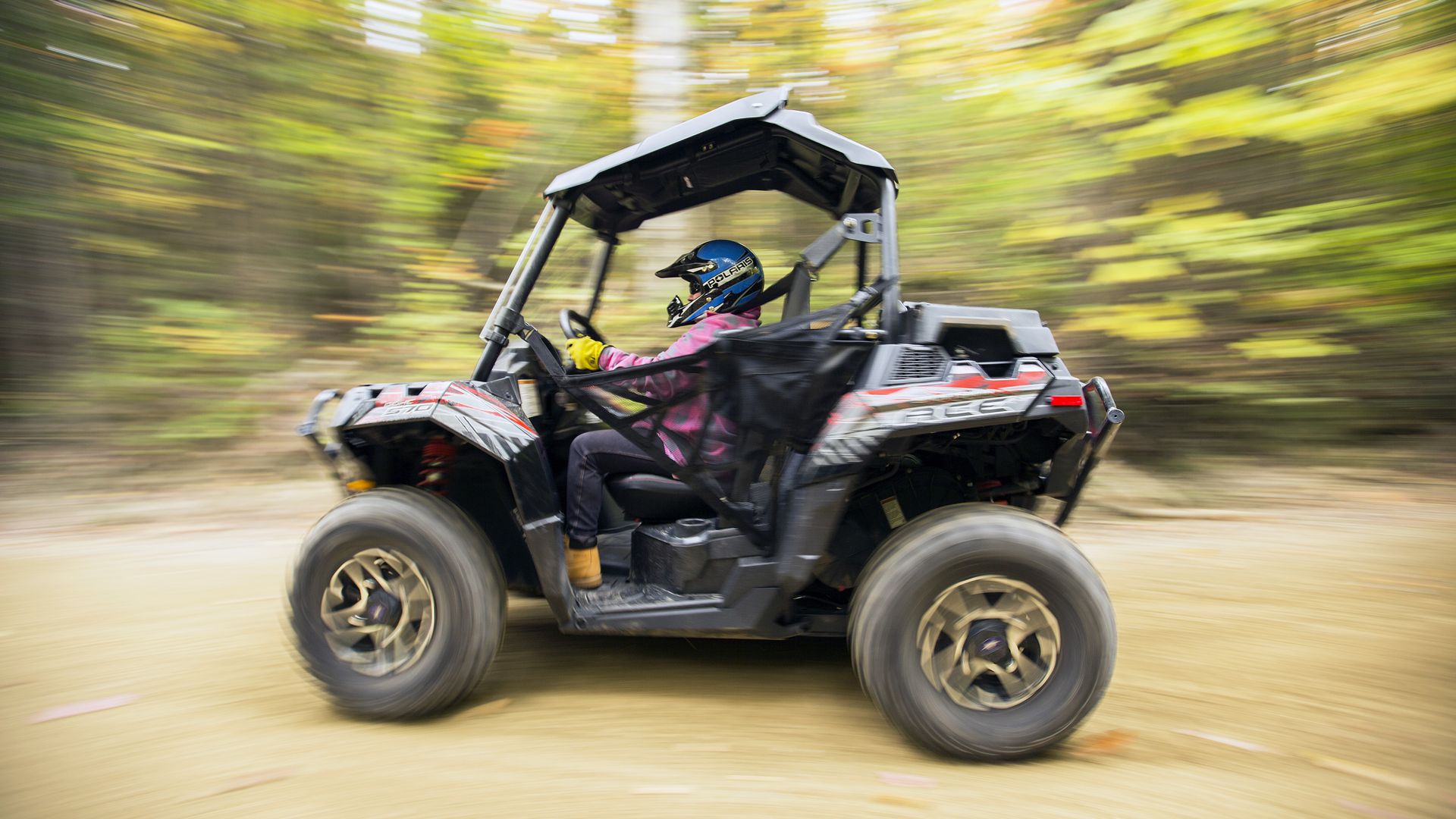 A woman driving an ATV with a blurred background behind her.
