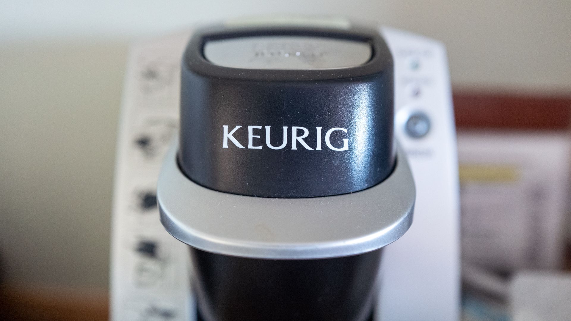 Close-up of a Keurig coffee maker's black dial with a silver ring, prominently showing the white KEURIG logo. The background is blurred.