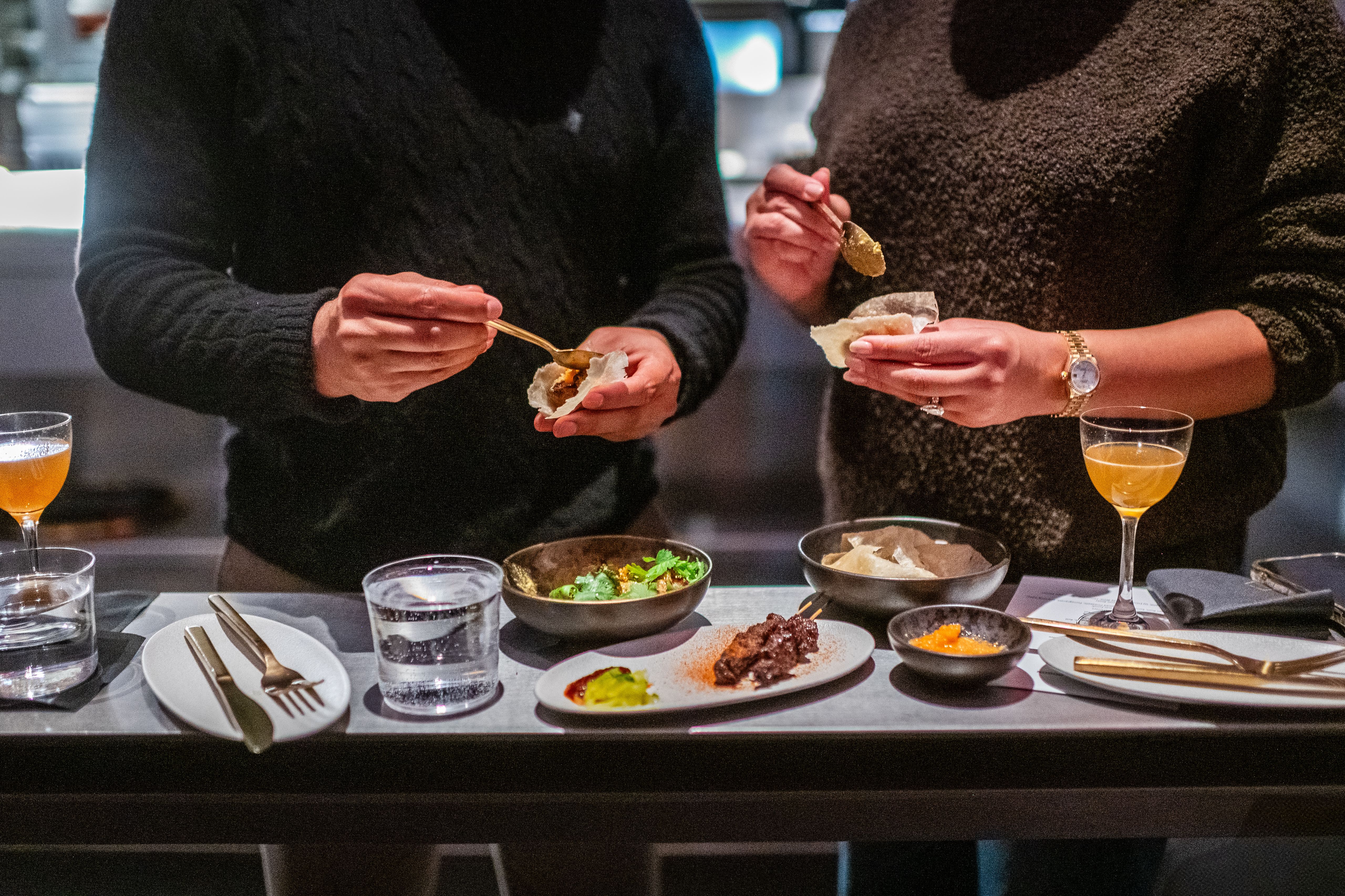 Two people at a standing dining bar with cocktails and handheld dishes