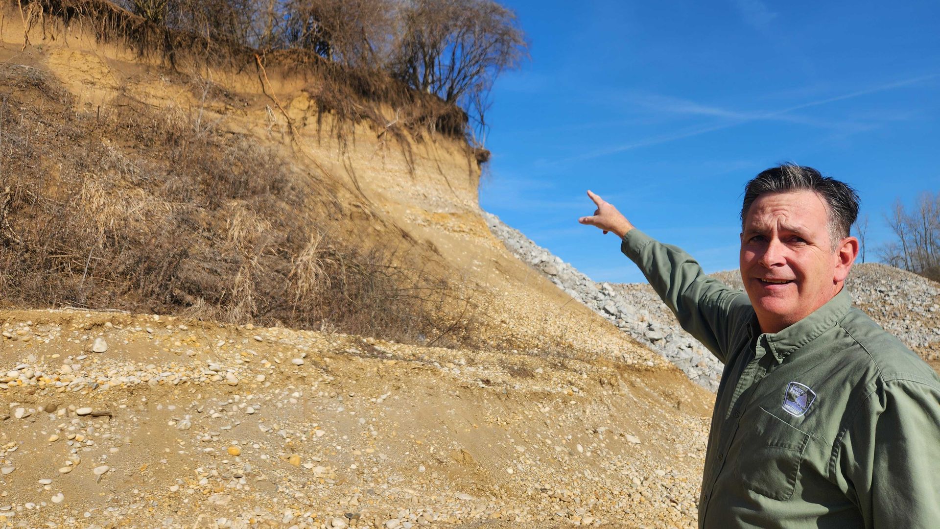 A parks director points at a rocky hill and trees.