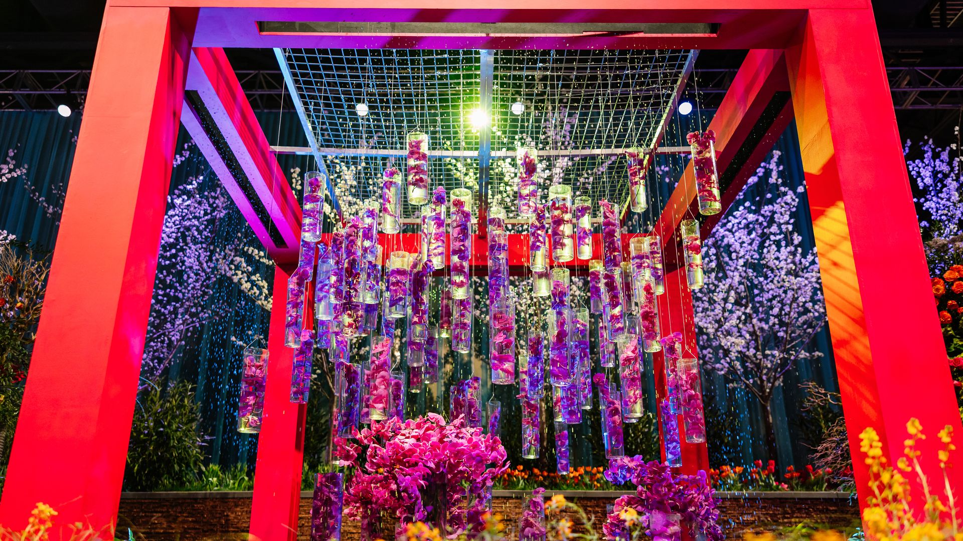 A vibrant floral installation, including hanging cylindrical glass vases filled with purple flowers, at the Philadelphia Flower Shower.
