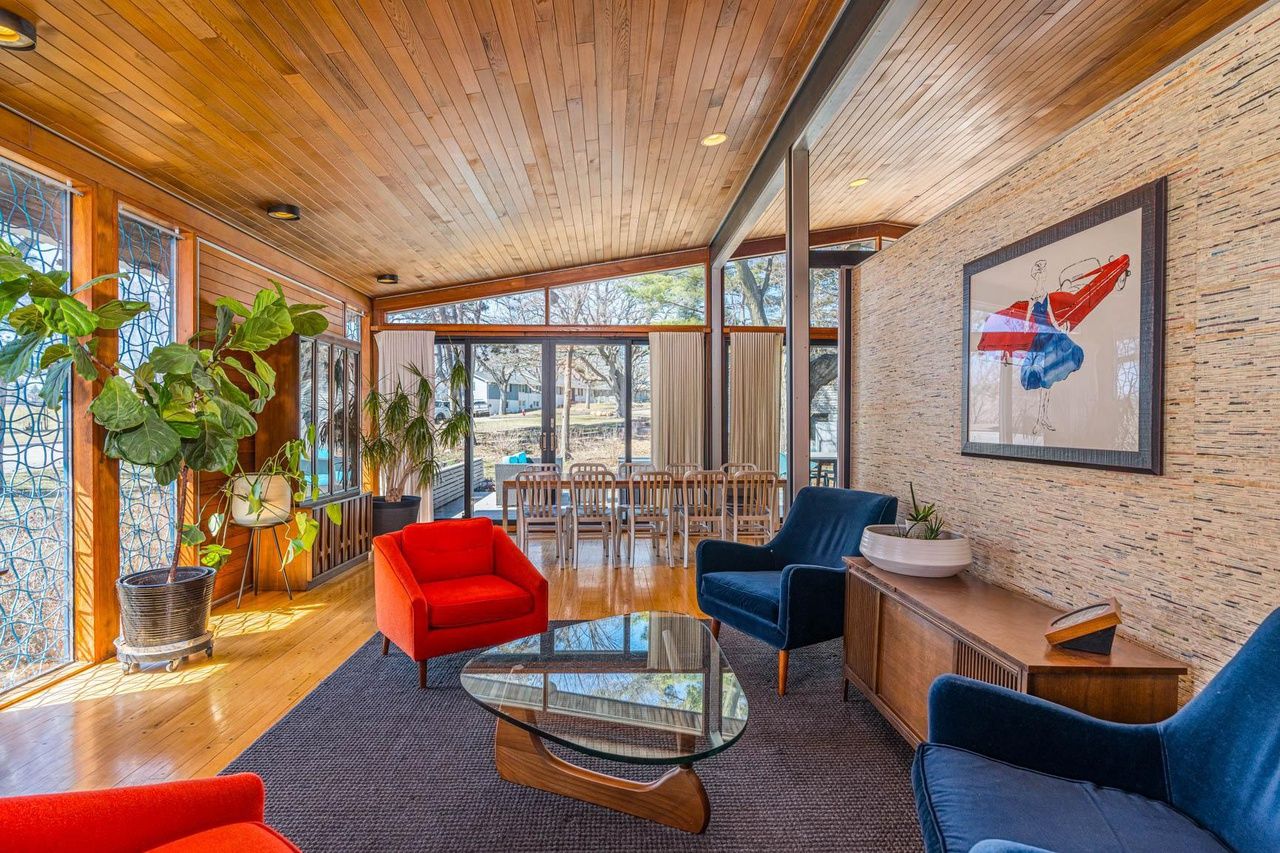 A mid-century modern style home with wooden ceilings andb lue and red furniture. 