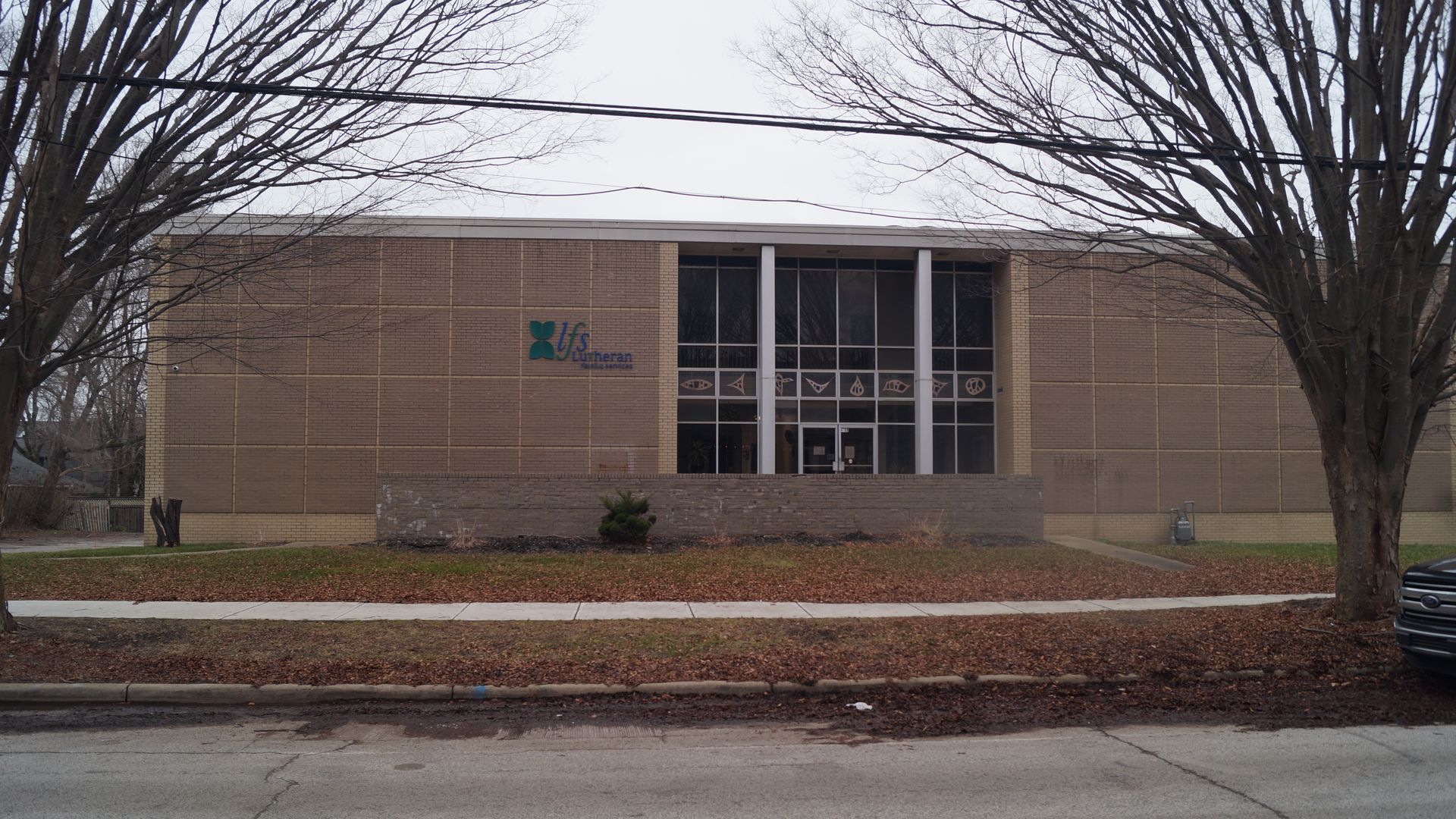 Exterior photos of beige brick building in autumn, framed by two leafless trees