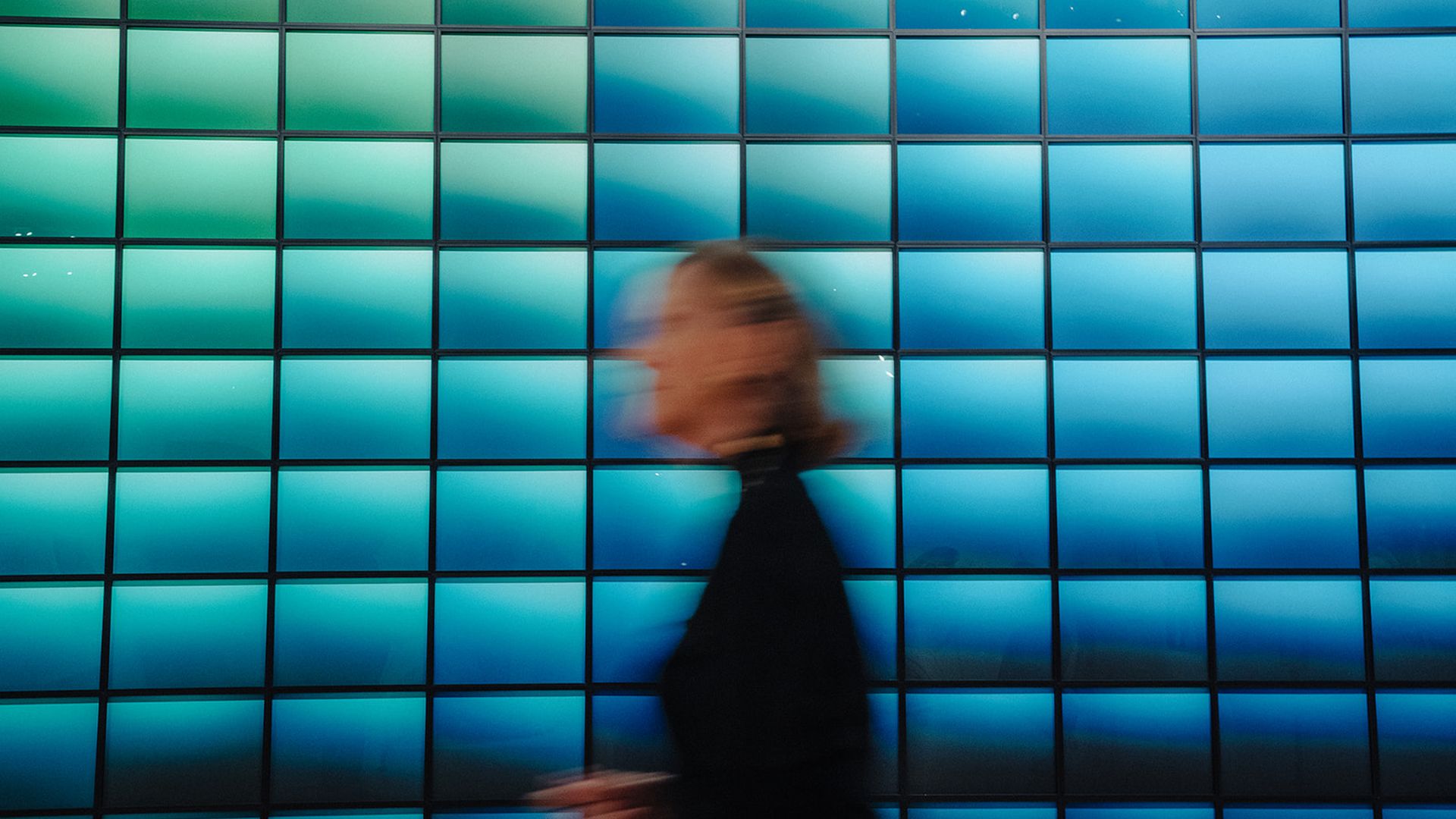 A person walks past a wall of green and blue gradient images.