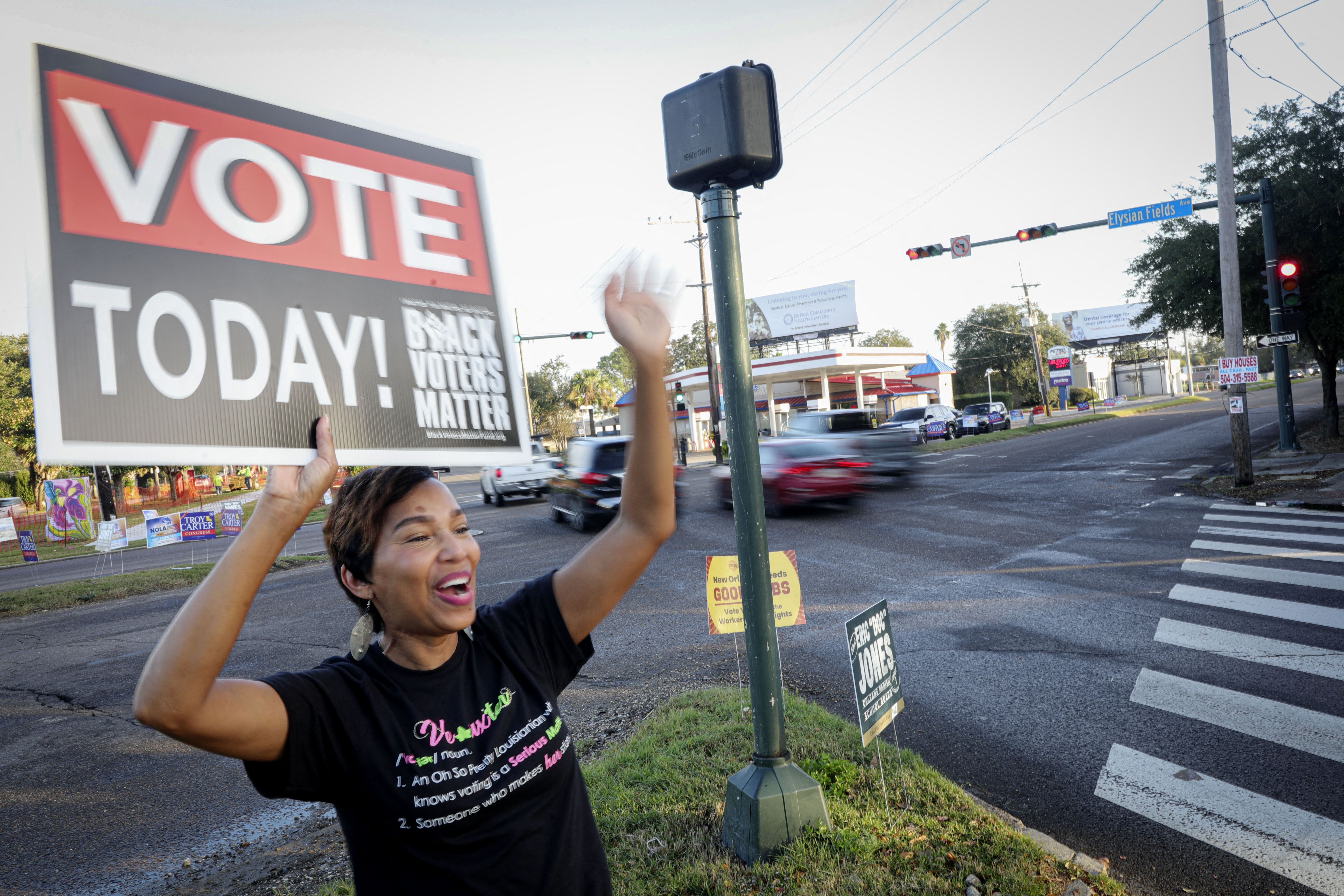 woman waves on street holding sign that reads vote today