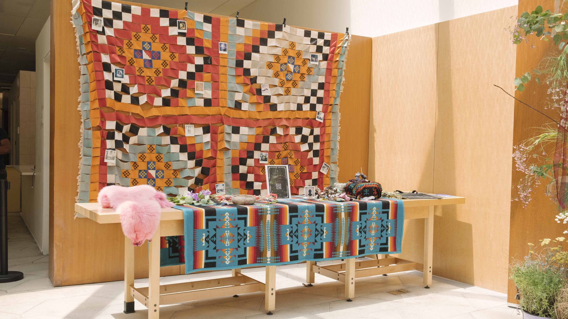 a table with fabrics and instructions. A fabric quilt is hung in the background with many bright colors.