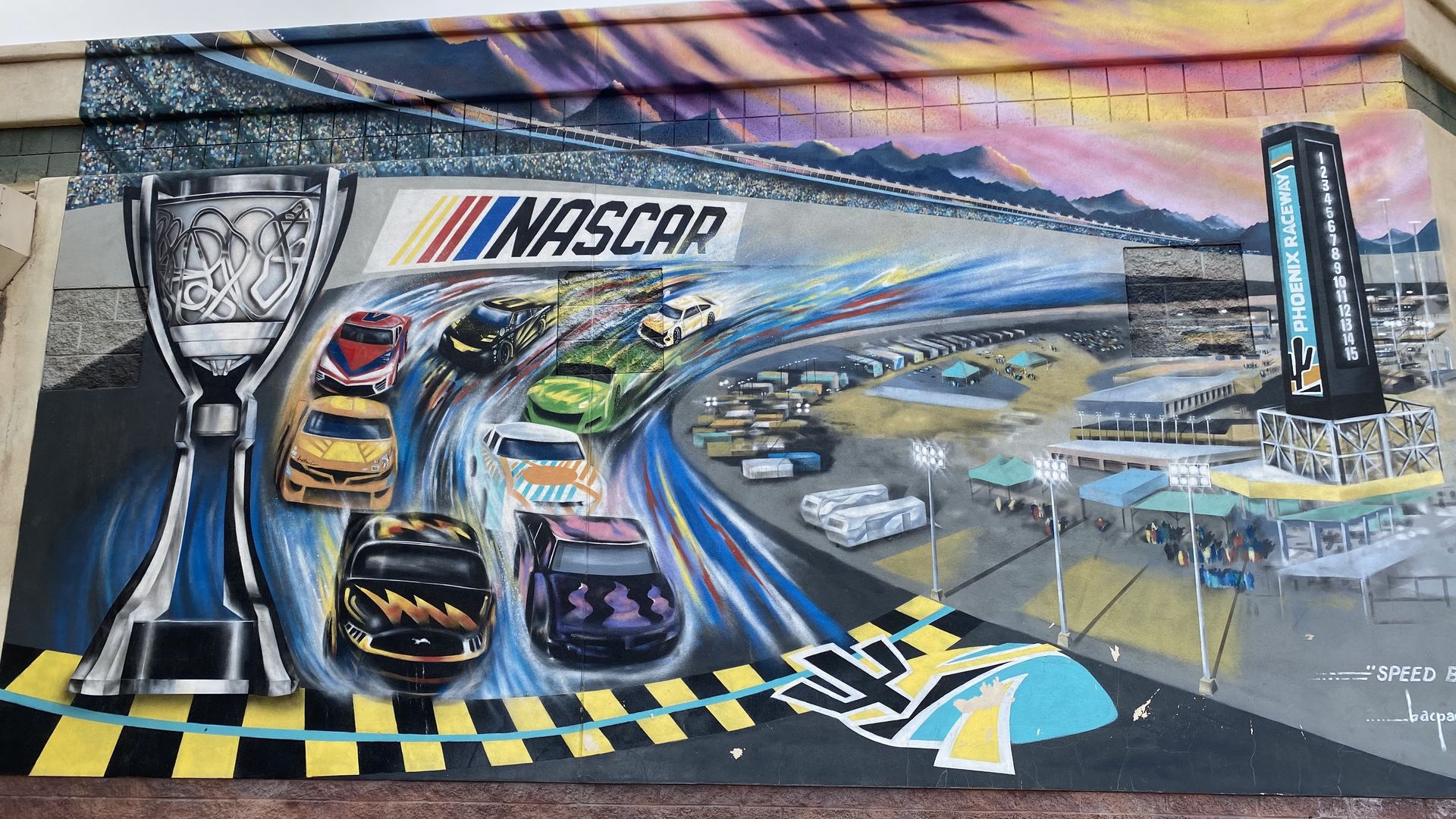 A mural depicting cars racing around a track with a trophy and the word NASCAR.