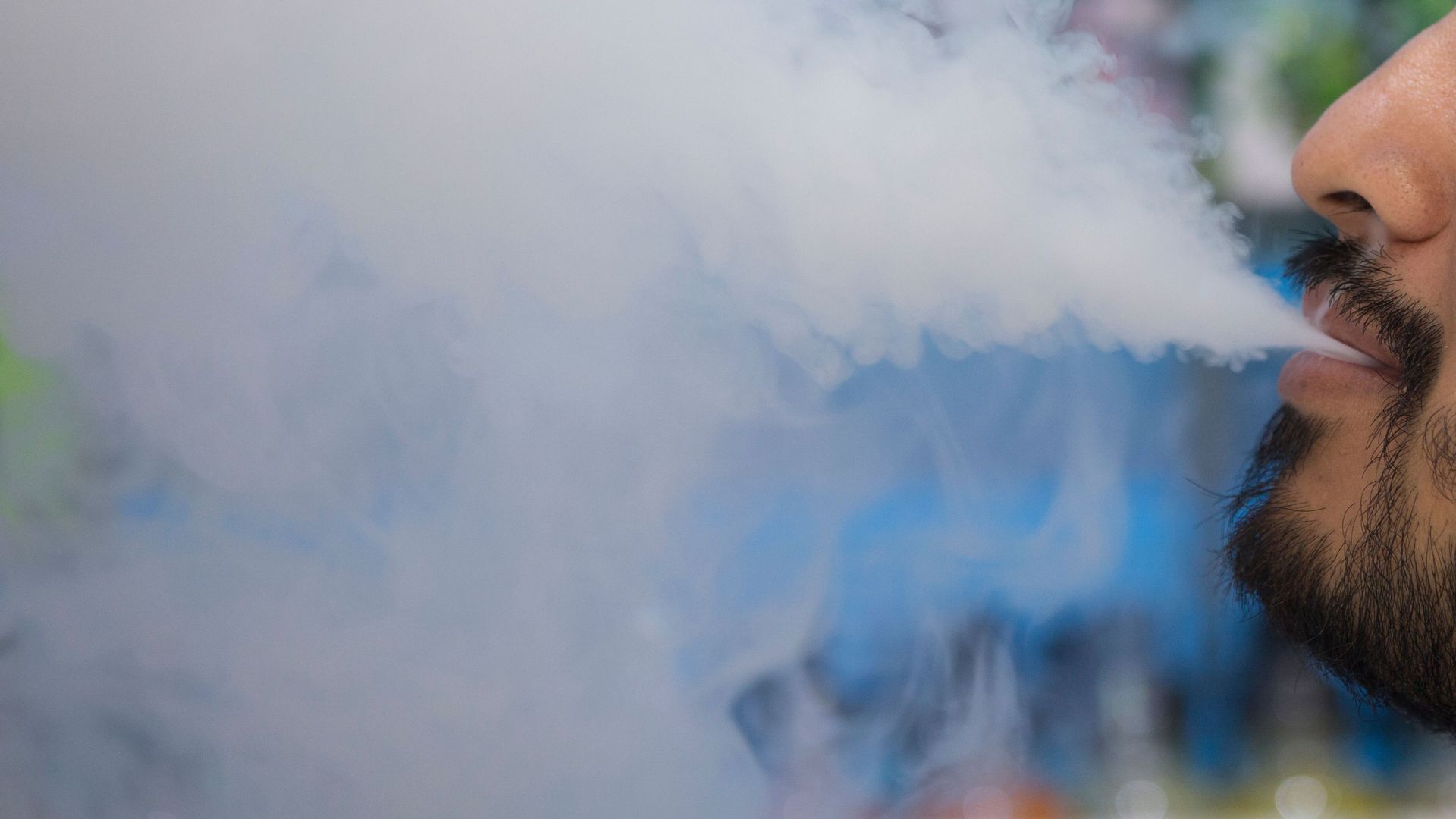 In this image, half of a man's bearded face is visible as he blows a large cloud of smoke to the left.