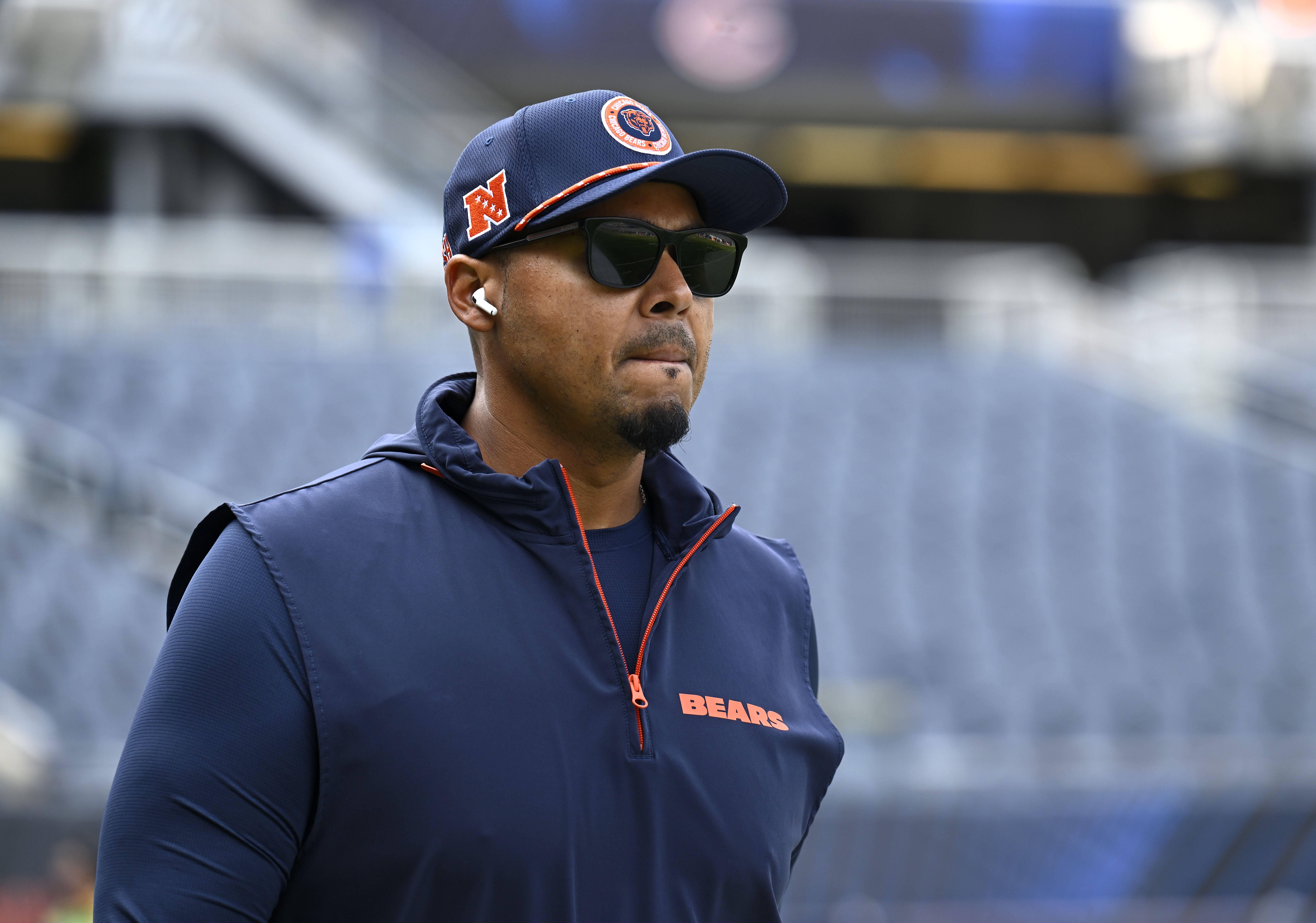Phot of a man in a "Bears" jacket watching a football game from the sidelines.