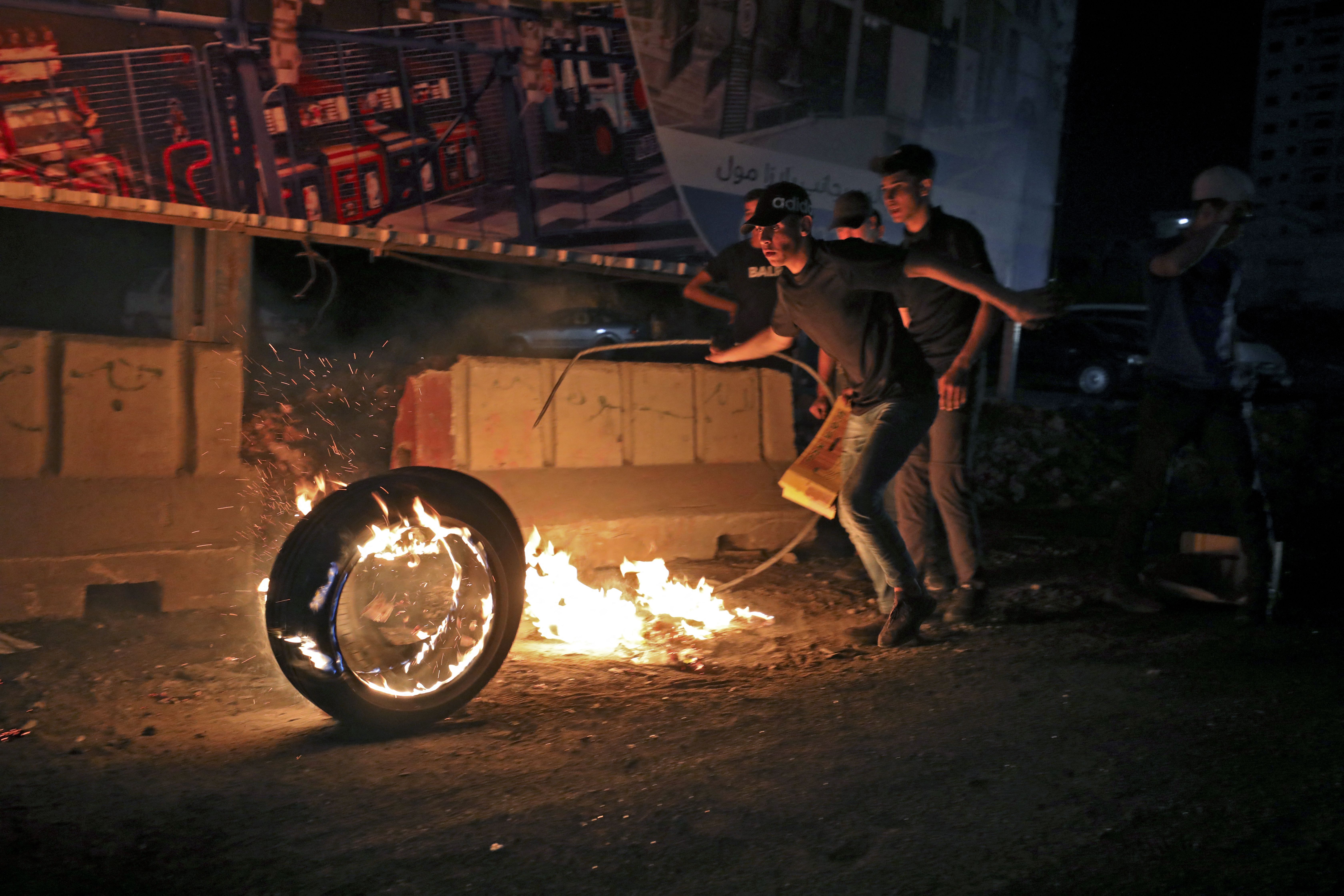 Palestinian protesters roll a burning tyre amid clashes with Israeli security forces at the Qalandia checkpoint between the West Bank town of Ramallah and Jerusalem on May 8
