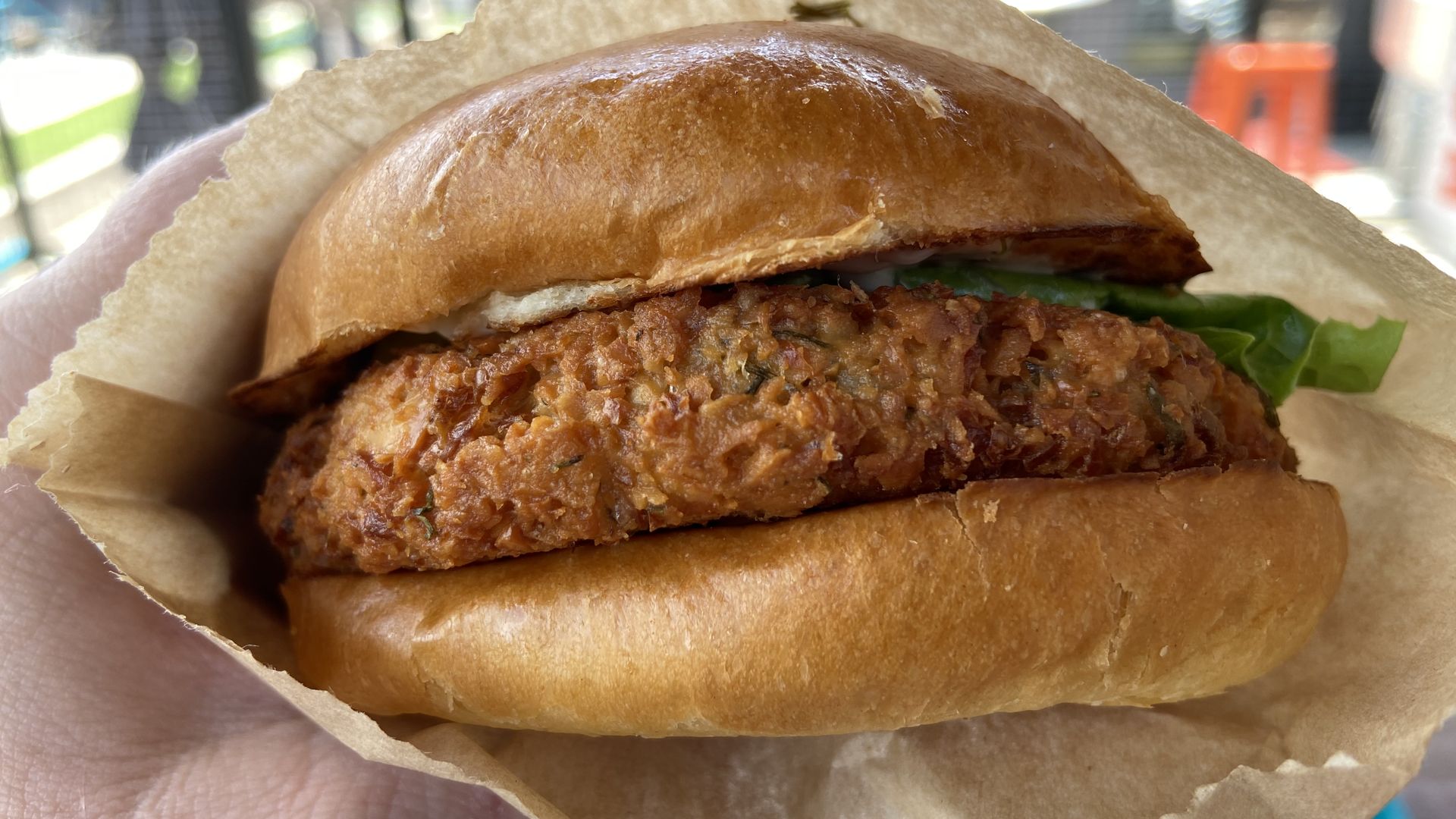 A close-up of a hand holding vegan chicken sandwich in a buttery bun