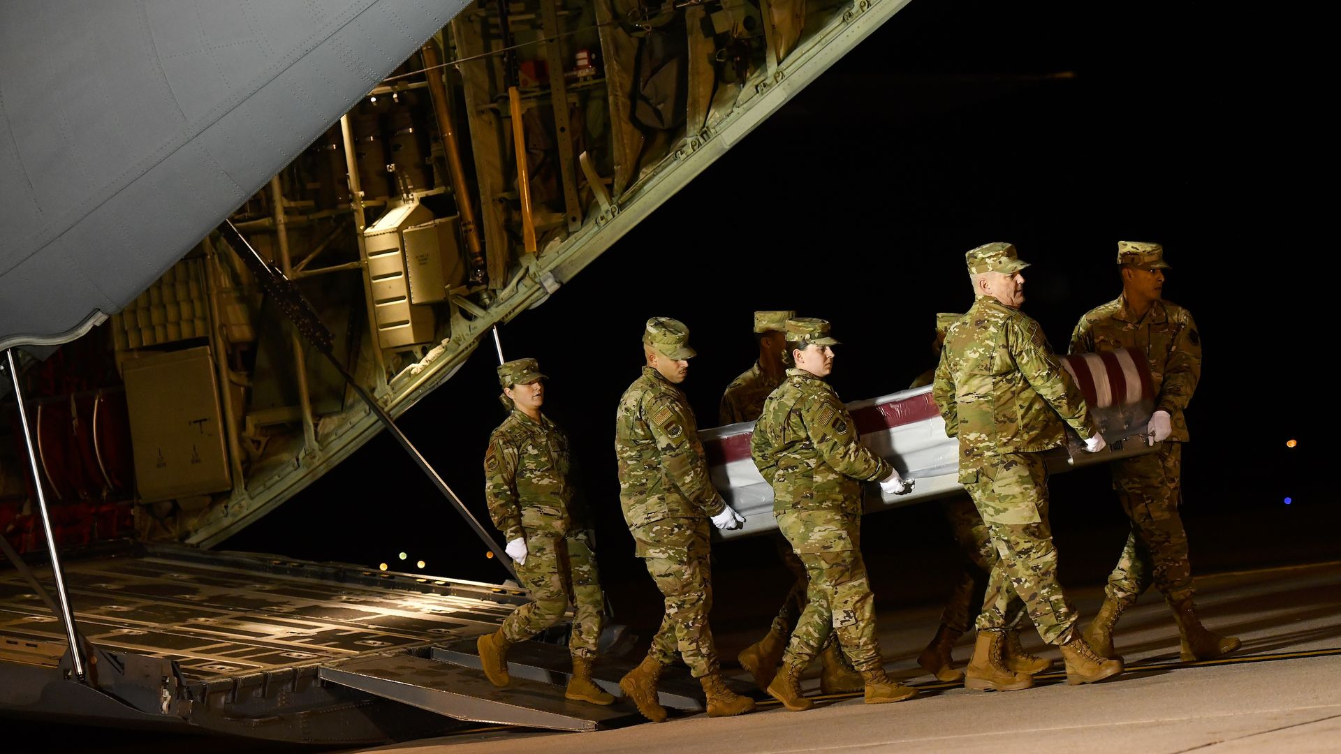 Military personnel carry a transfer case for a service member who died in the shooting.