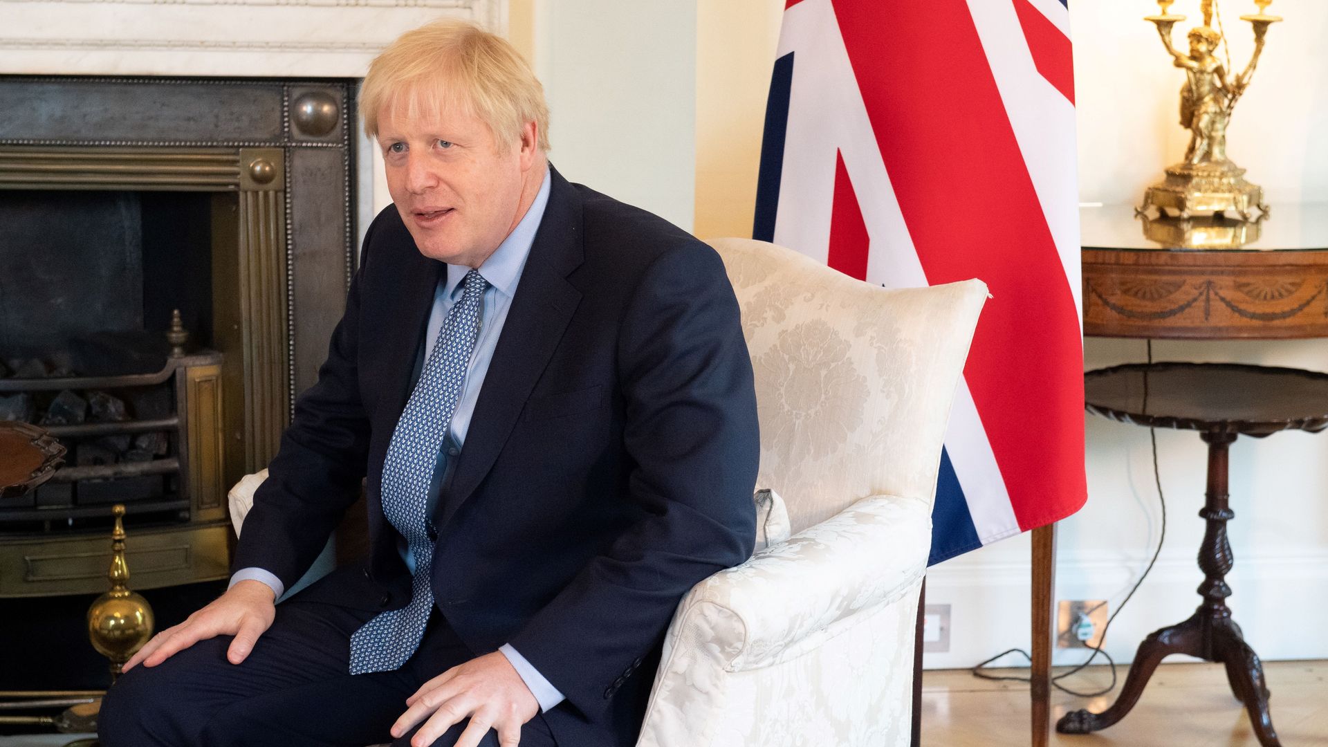 In this image, Boris Johnson sits in a chair with the British flag behind him.