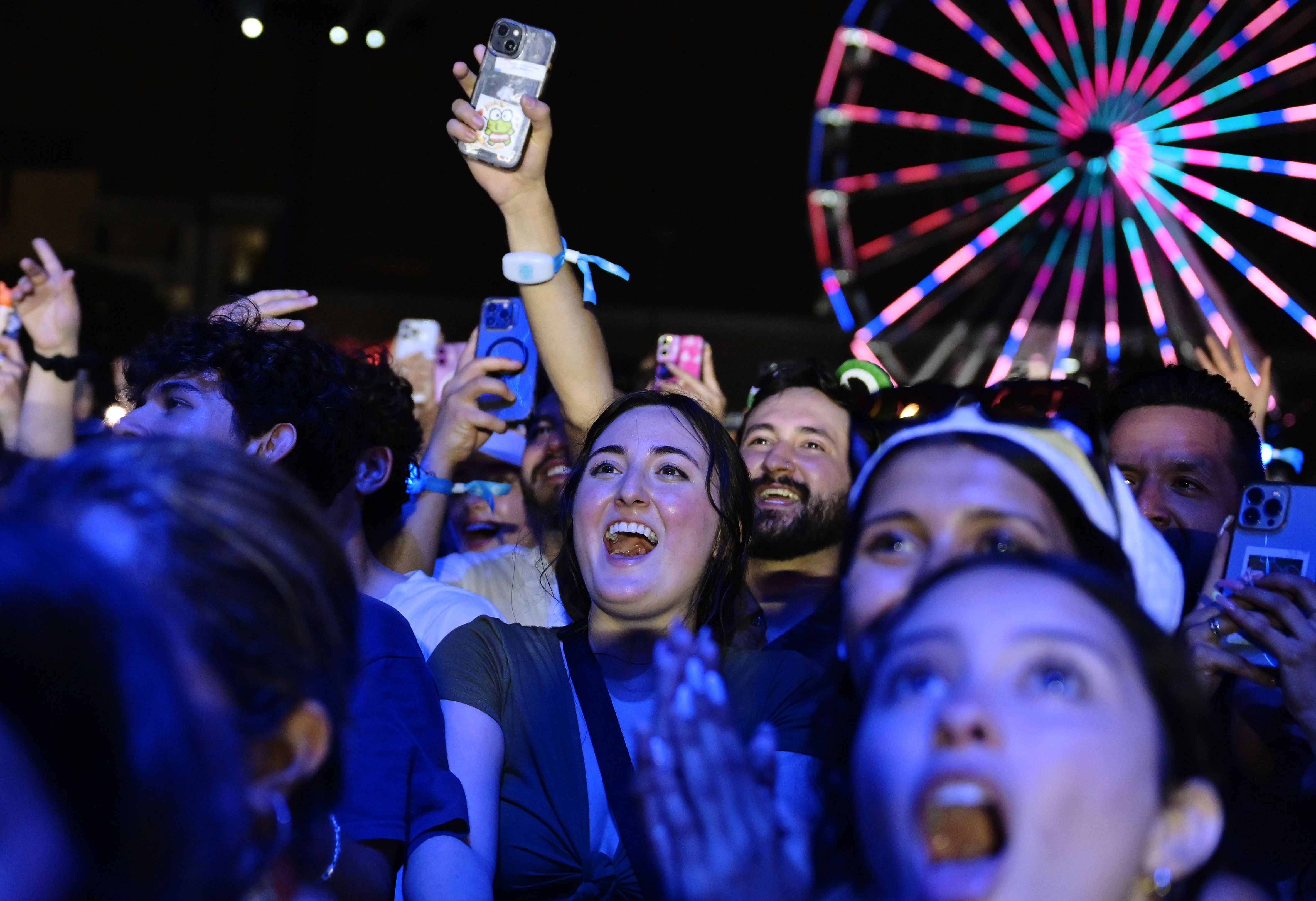 A woman seen smiling with a light-up ferris wheel behind her.
