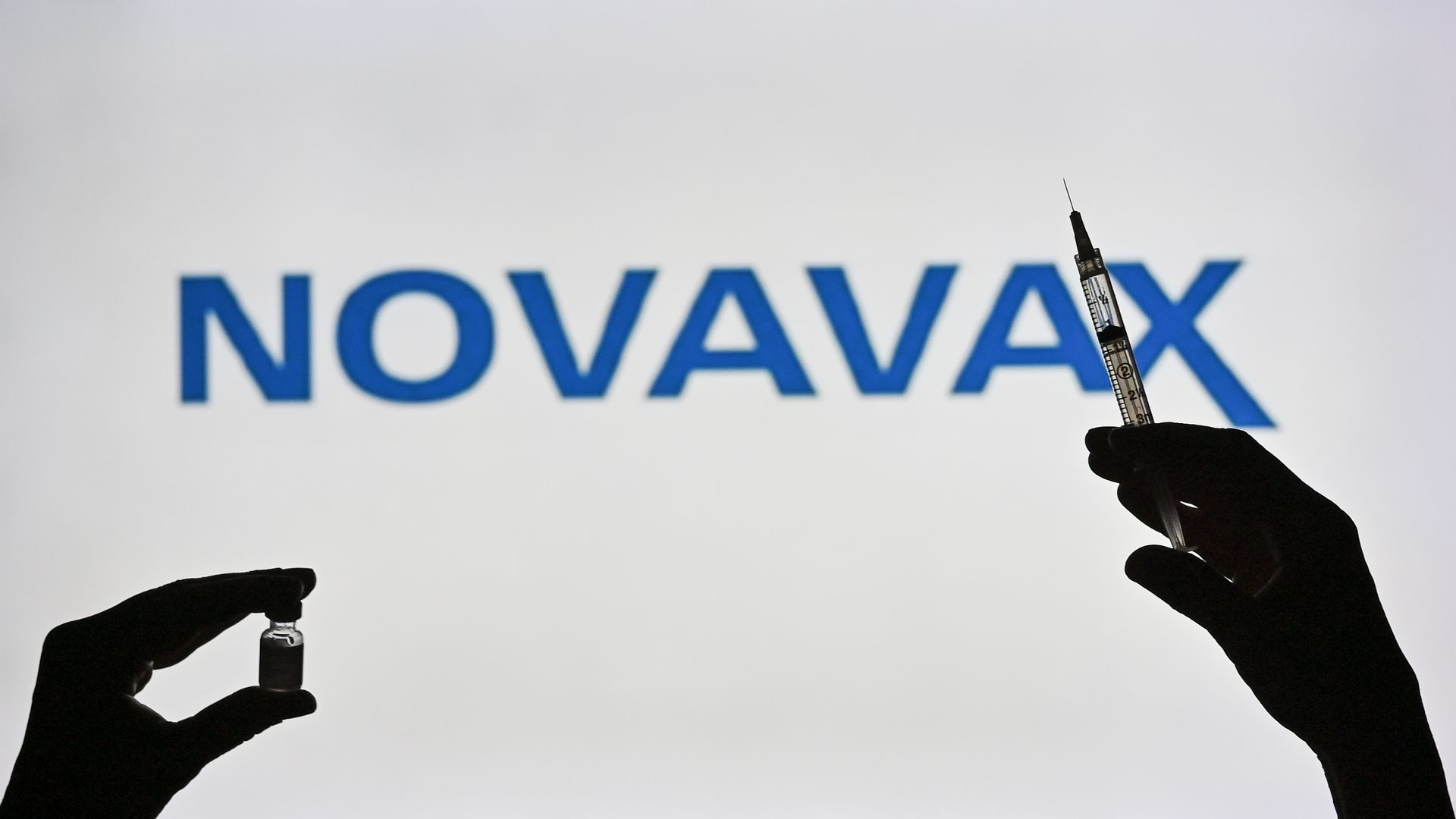 Picture of the Novavax logo with two hands in front of it holding a vial and a syringe 
