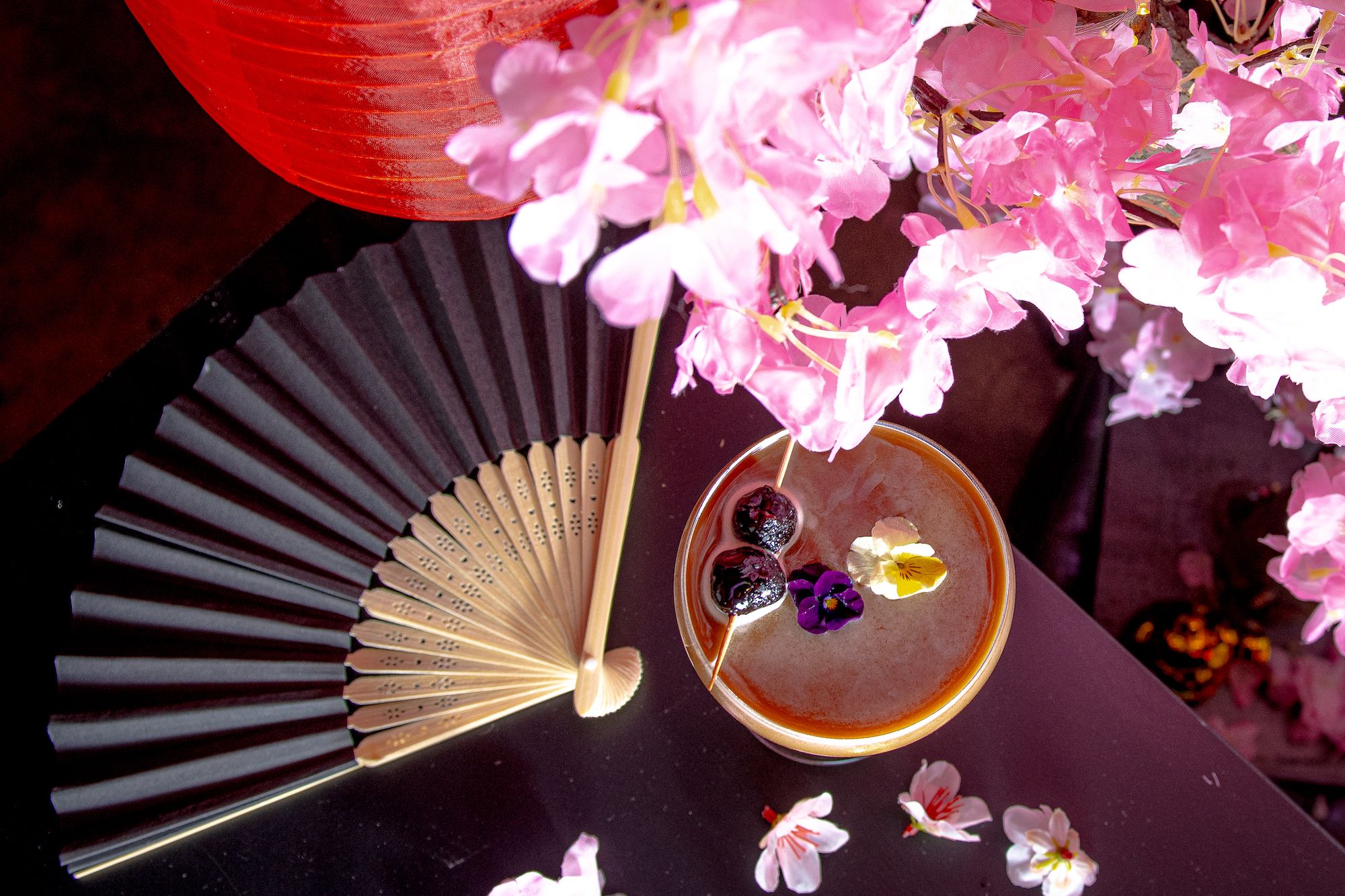 A table with a Japanese fan, cocktail with flowers on top, and cherry blossom branches