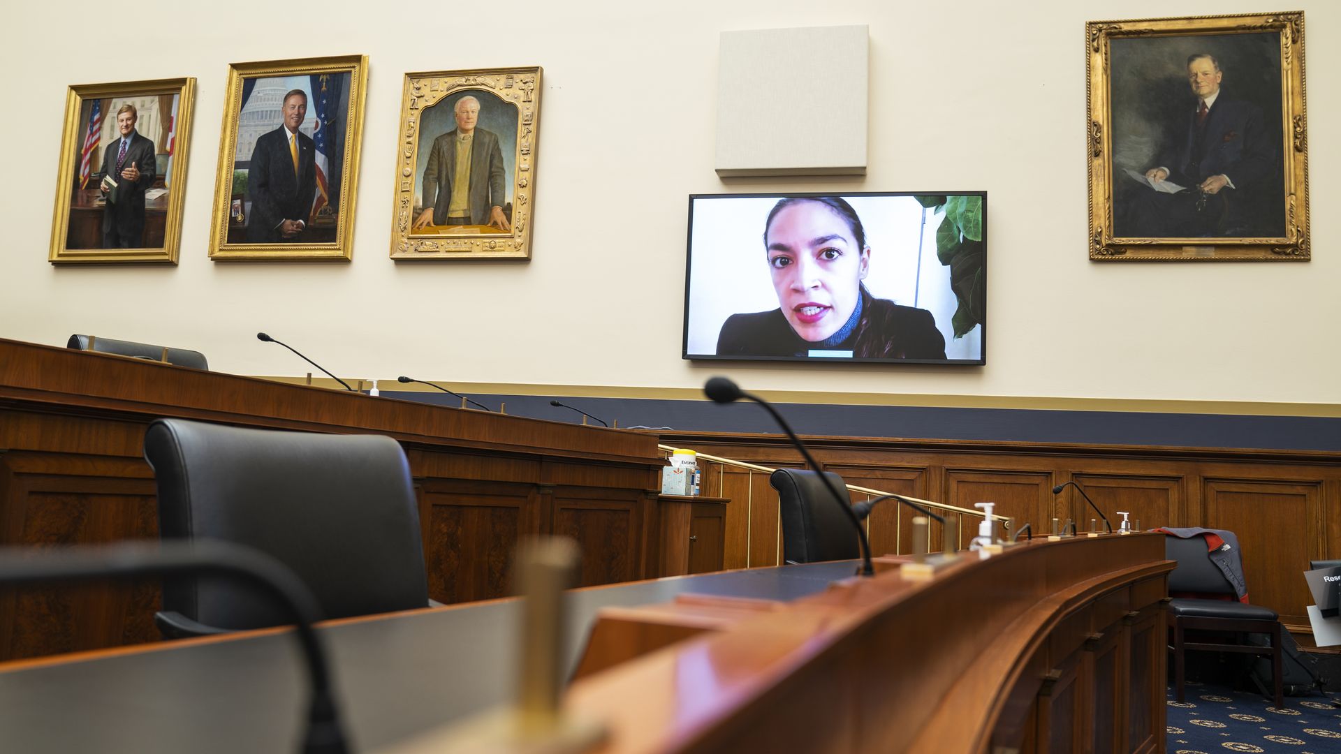 Rep. Alexandria Ocasio-Cortez is seen on a TV monitor as she beams into a congressional hearing.
