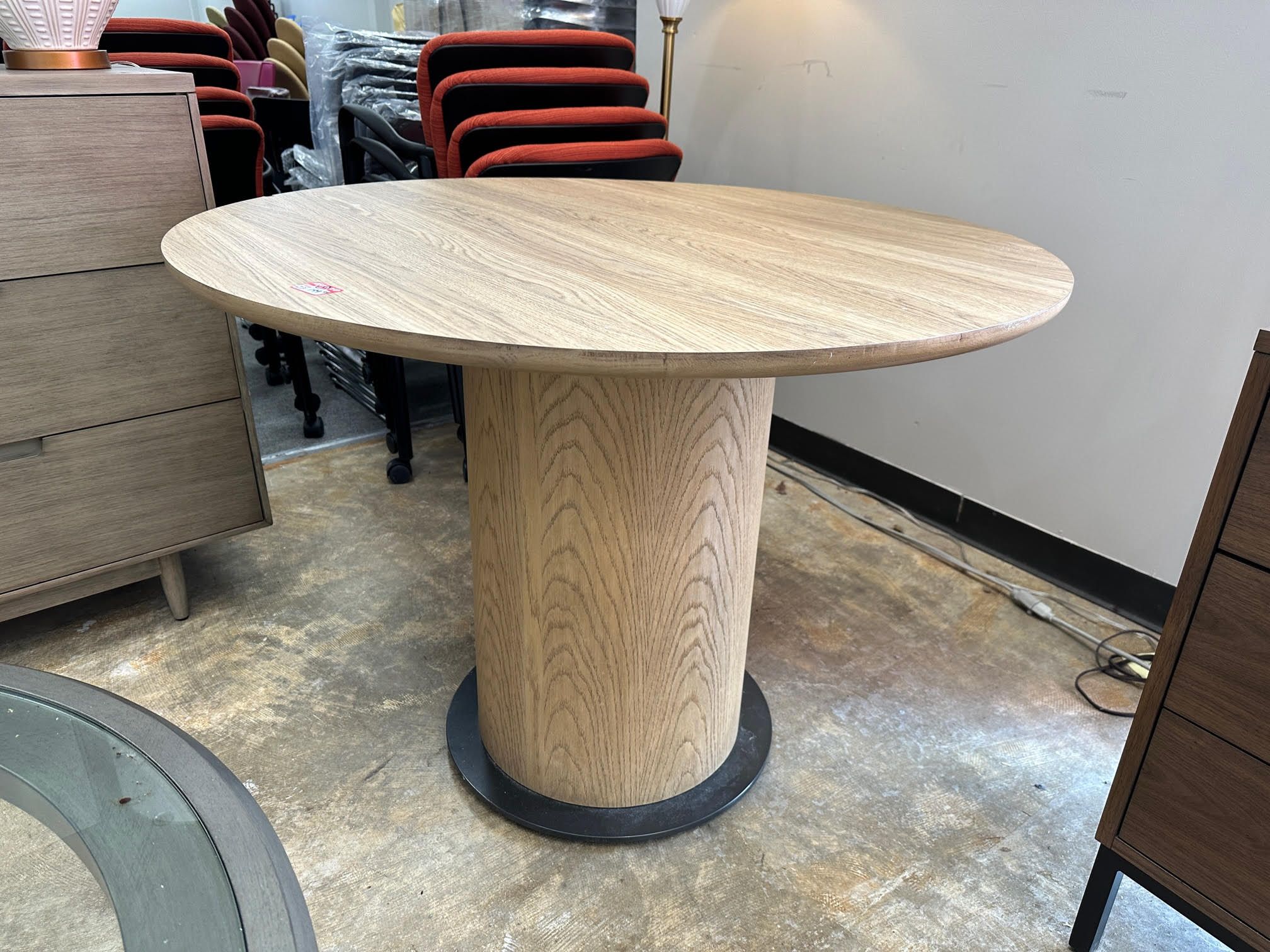 A wooden circular table with a cylinder-style base. 