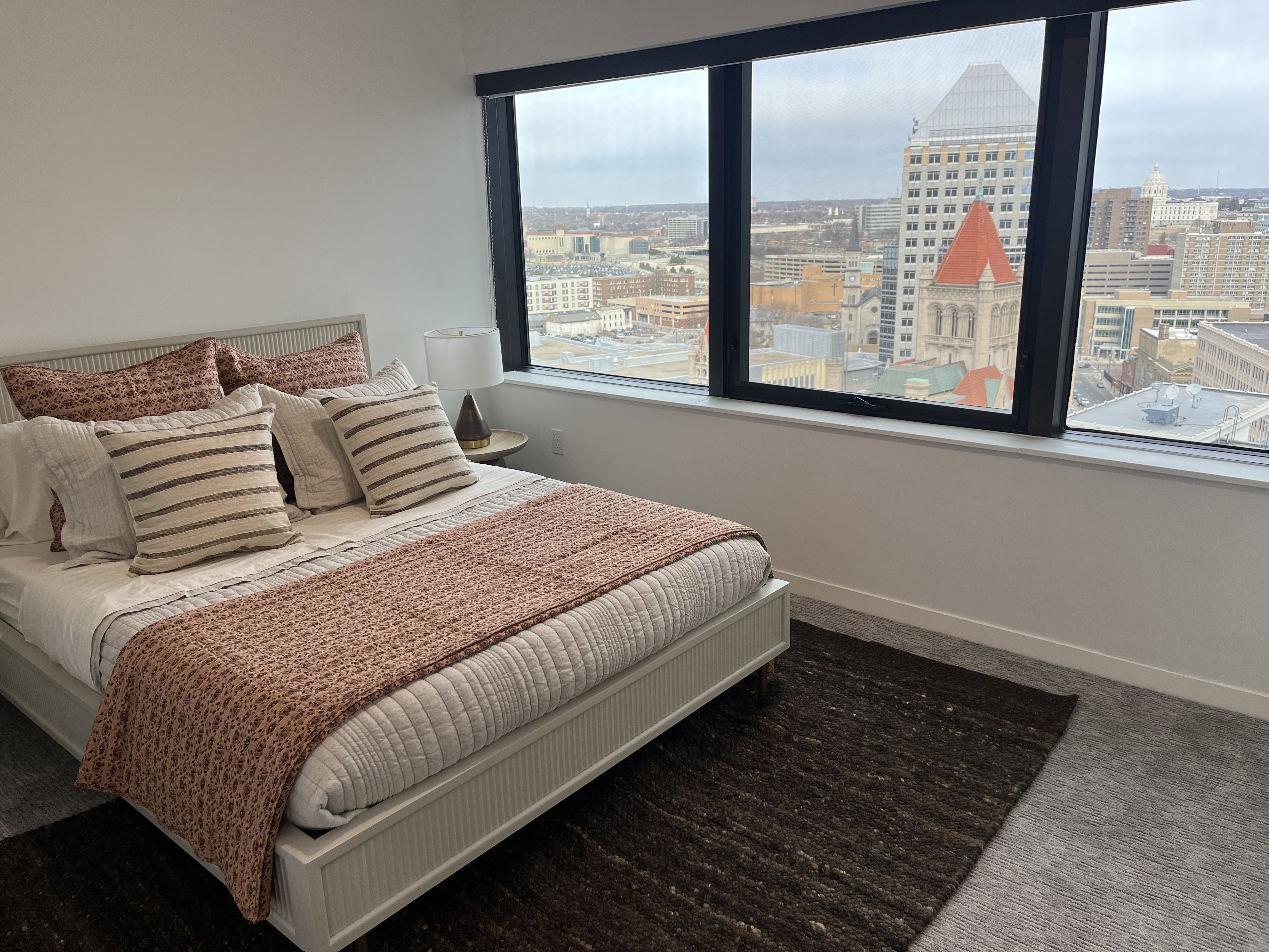 A photo of a bedroom with windows overlooking downtown
