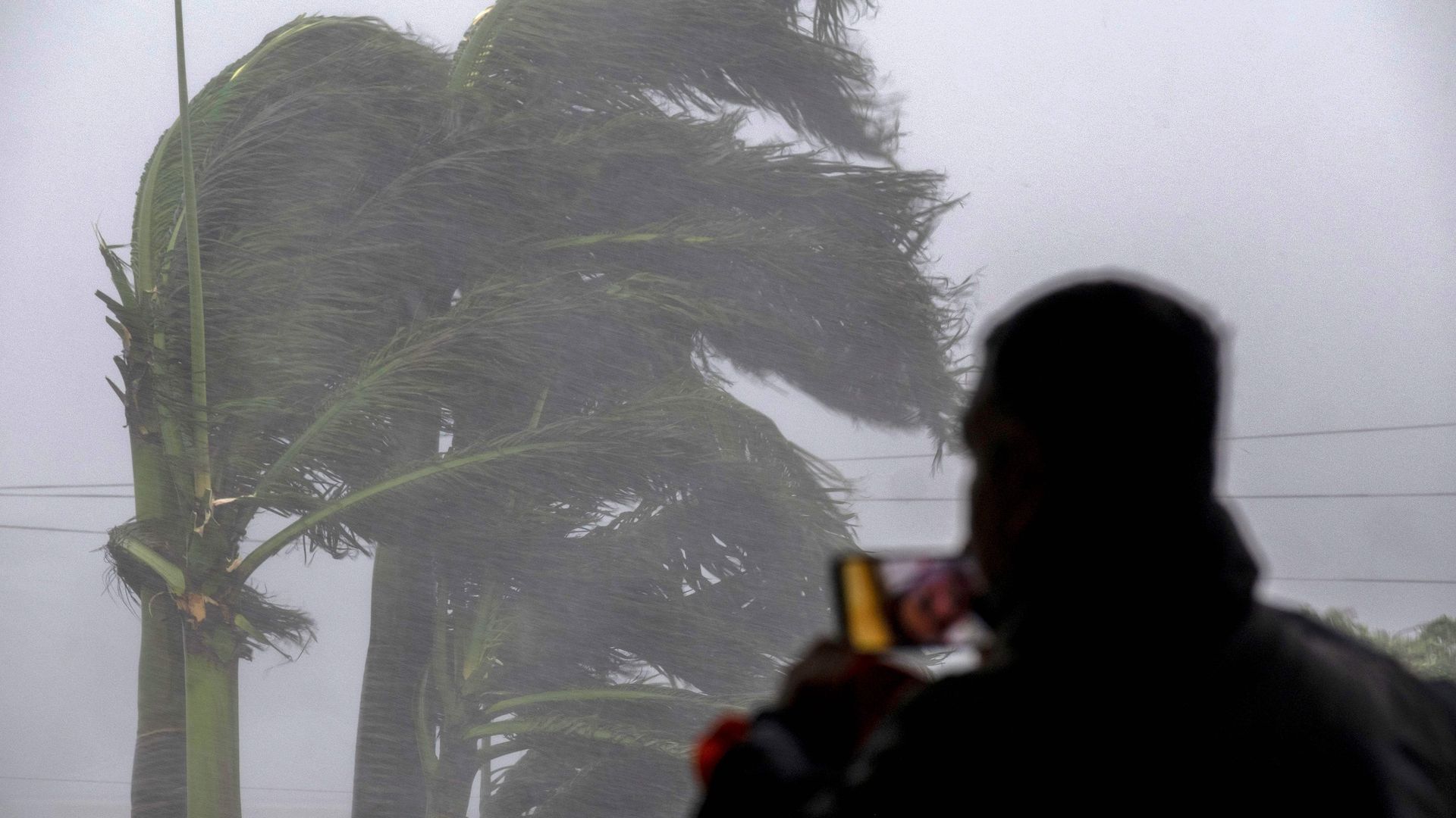 The silhouette of a person films Hurricane Ian outside on their phone.