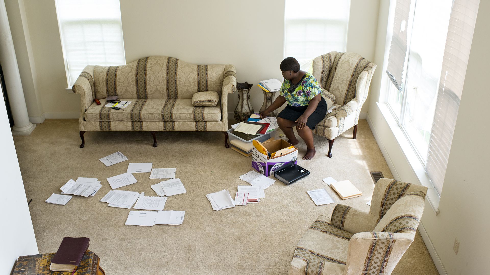 A woman sits in a room with papers scattered on the floor.