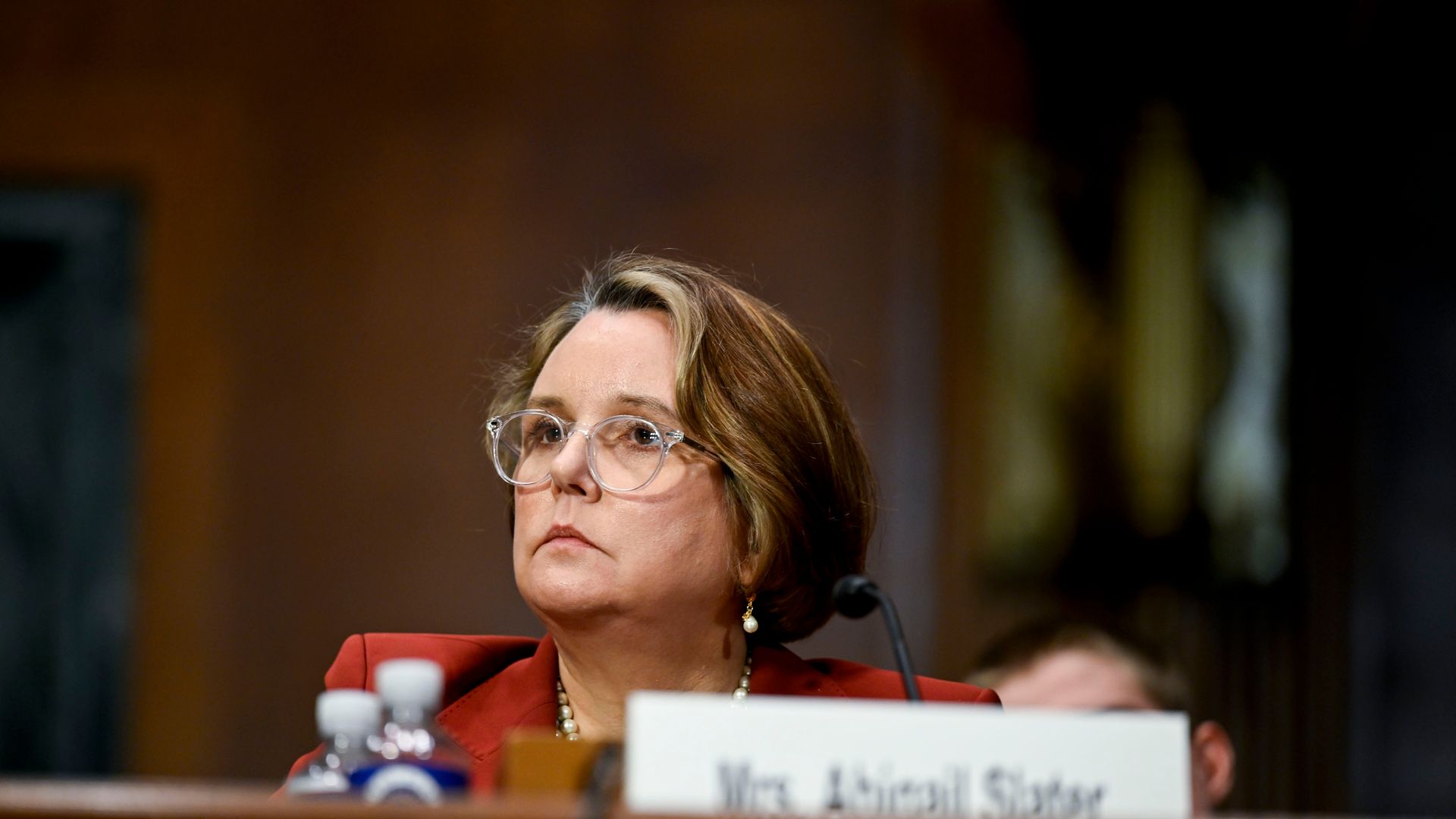 A person wearing glasses and a red top sits in front of a microphone