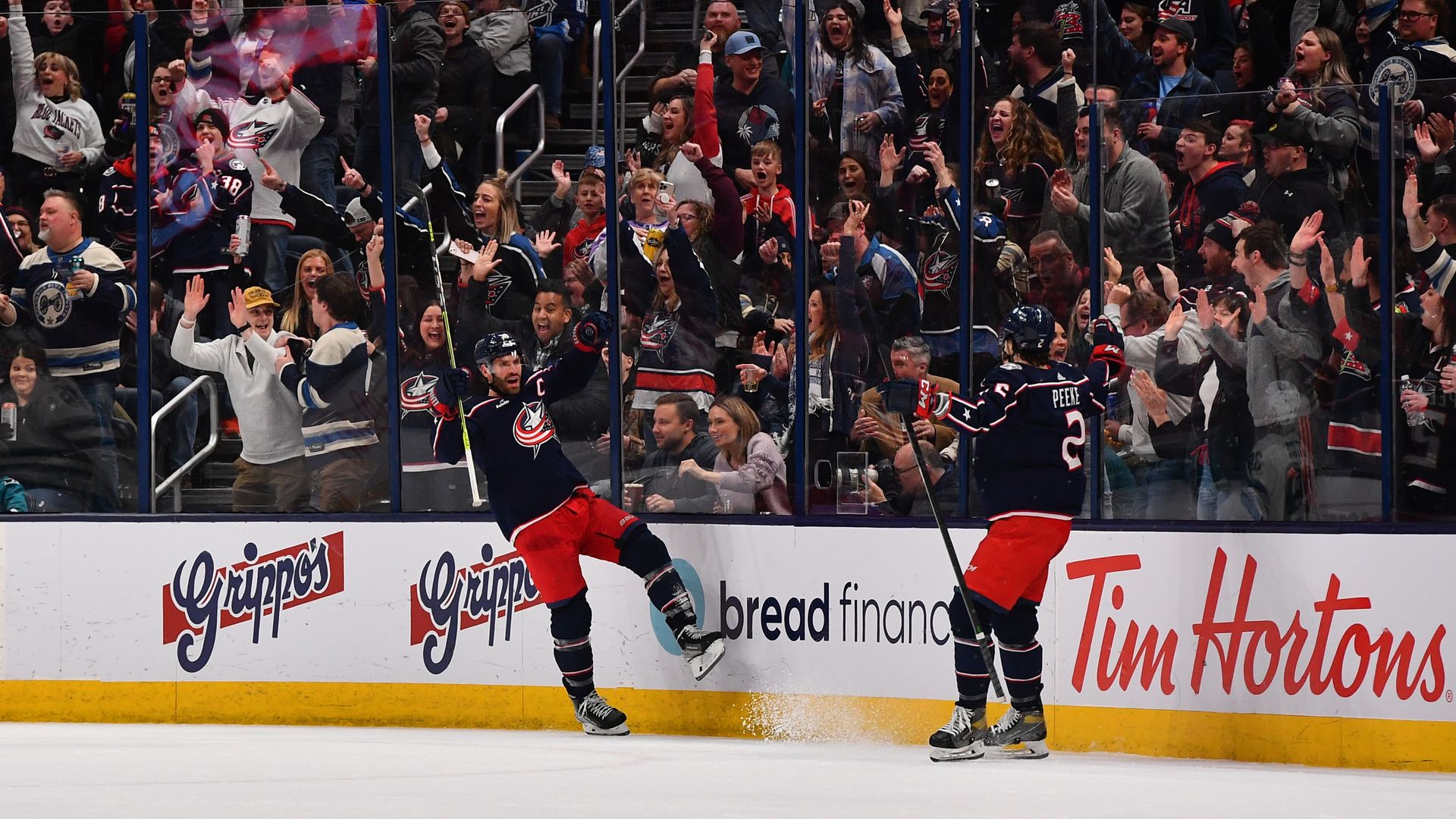 Boone Jenner celebrates with teammate Andrew Peeke after scoring a goal while fans cheer