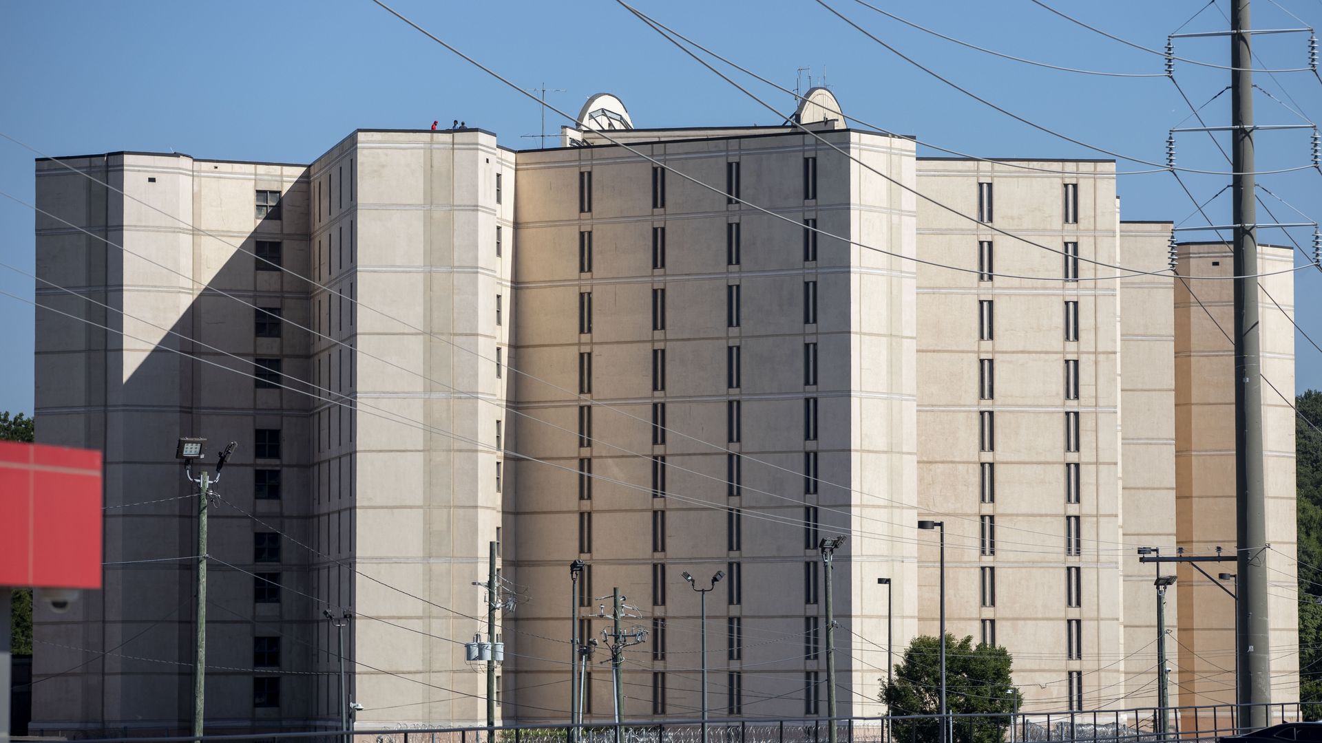 A large beige building with several towers and small, vertical-lined windows. Power lines and utility poles are in the foreground.