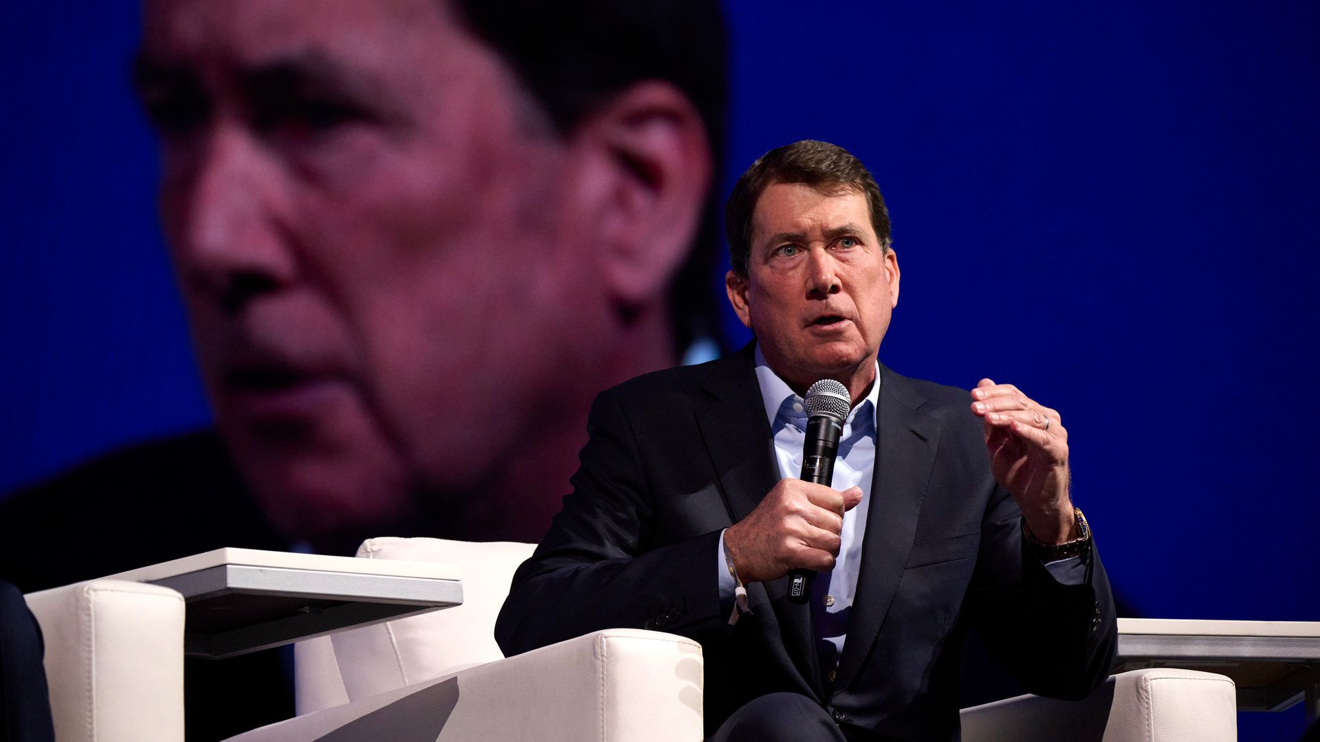 A man speaking at a conference, with his own image projected behind him. 